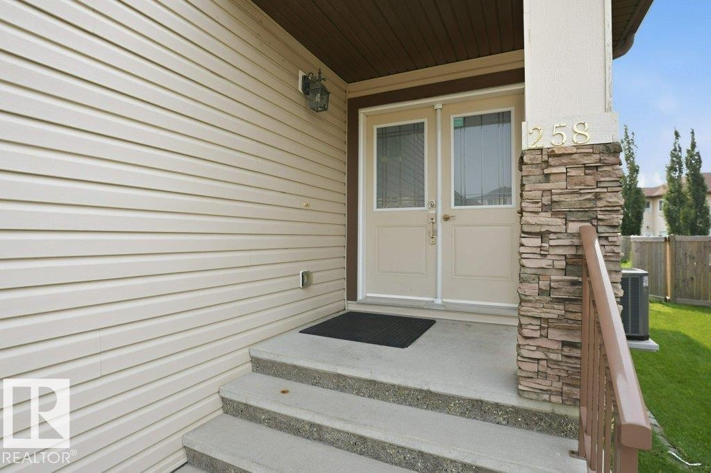 Entryway featuring double doors with decorative glass panels, stone veneer pillar, concrete steps, and a metal handrail - 258 Albany Drive Nw, Edmonton, AB - Outdoor With Exterior