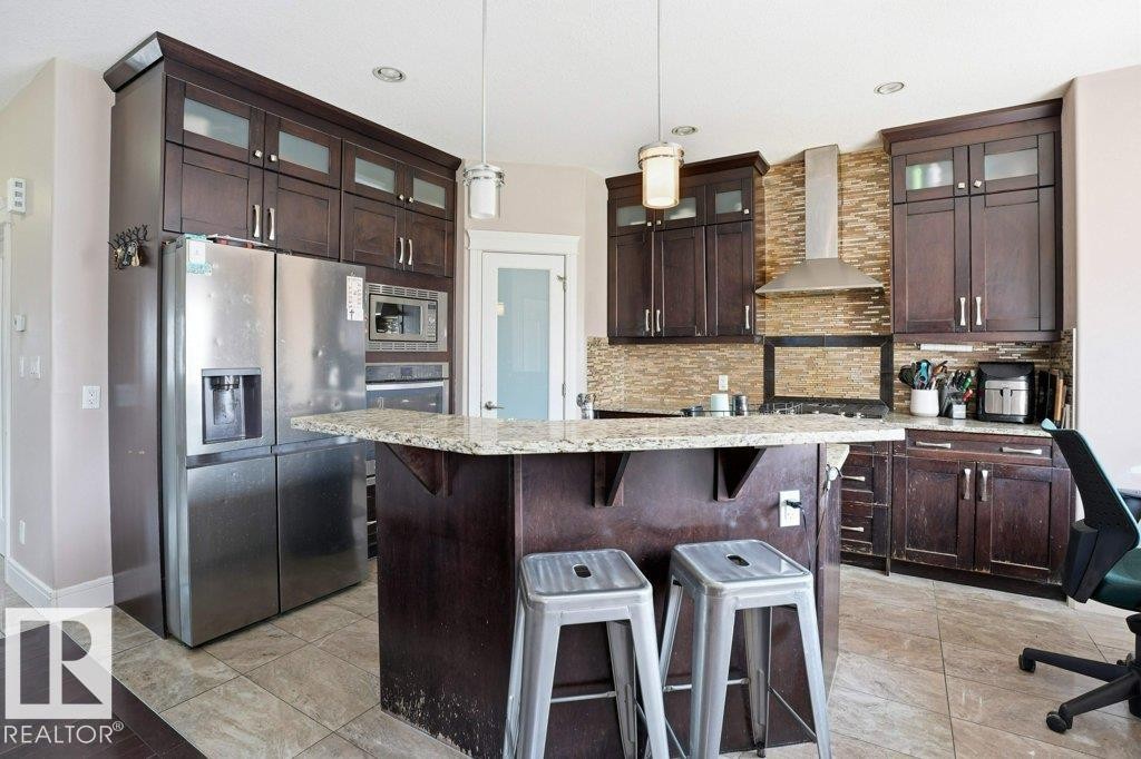 Kitchen featuring dark wood cabinetry, stainless steel appliances, a center island with a granite countertop, and a tiled backsplash - 258 Albany Drive Nw, Edmonton, AB - Indoor Photo Showing Kitchen With Upgraded Kitchen