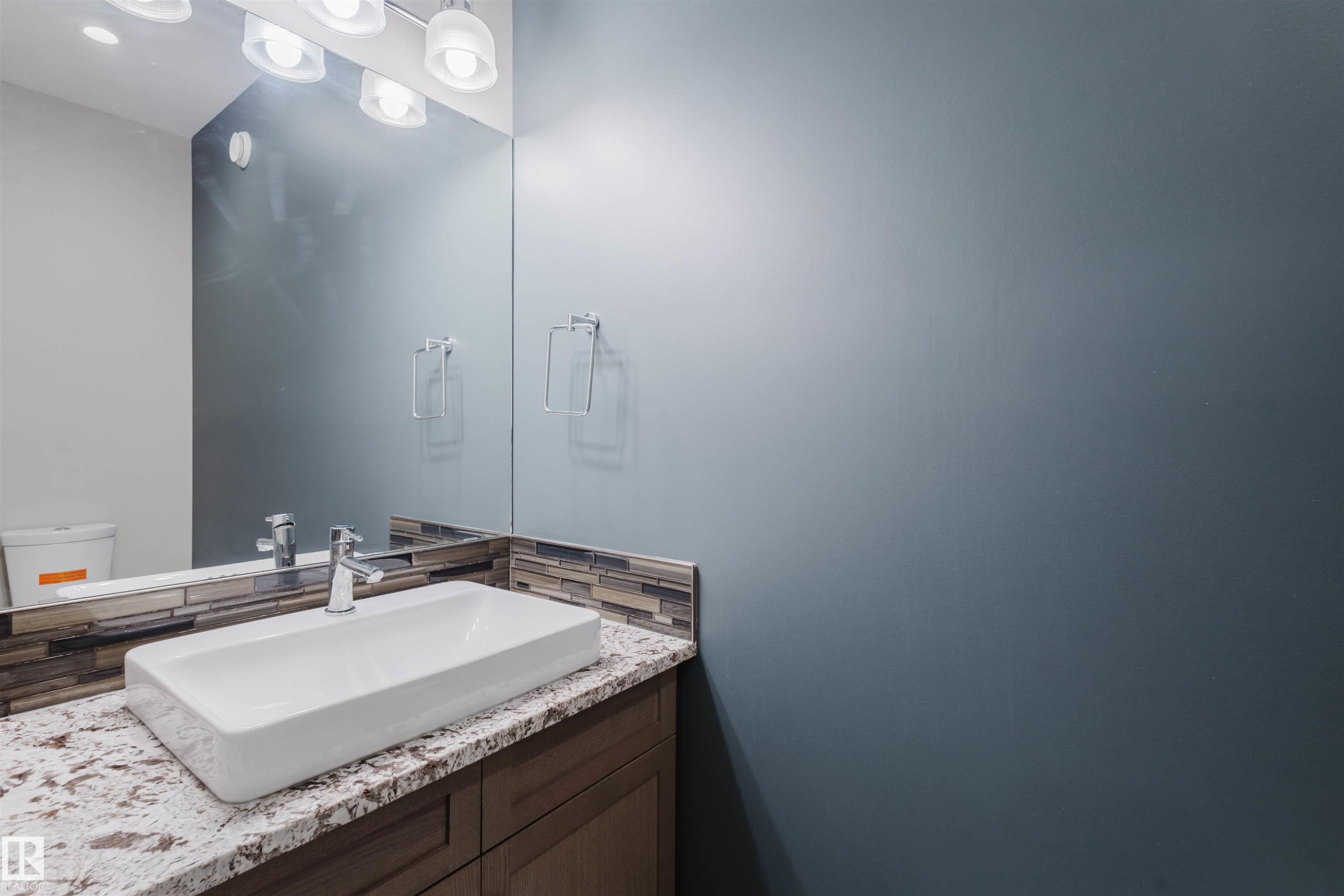 Modern vanity featuring a rectangular vessel sink, polished chrome faucet, stone-look countertop, and a mosaic tile backsplash - 4125 Kennedy Green Sw, Edmonton, AB - Indoor Photo Showing Bathroom