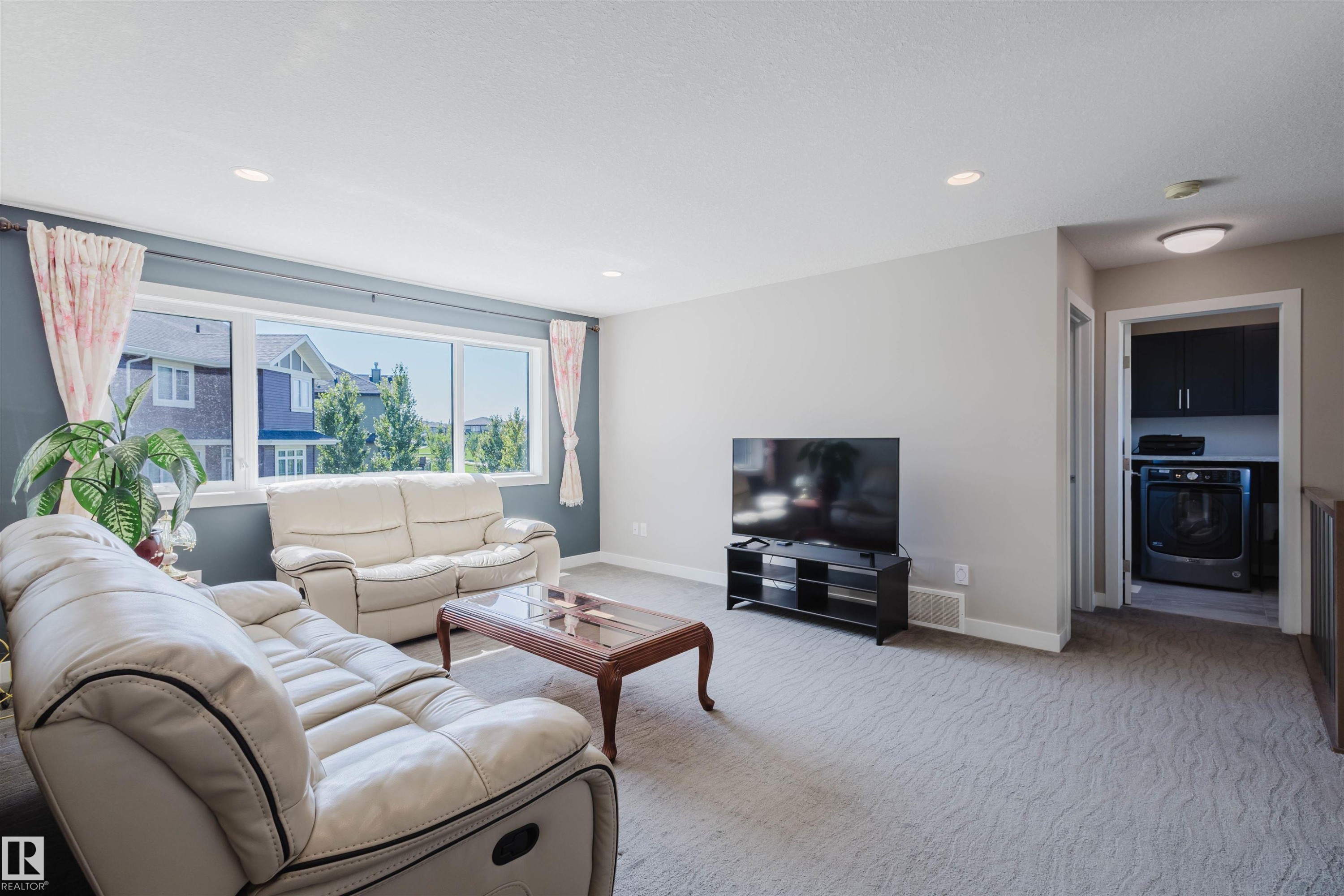Carpeted living area featuring a large window, recessed lighting, and a dedicated laundry alcove with built-in cabinetry and an integrated washer and dryer - 4125 Kennedy Green Sw, Edmonton, AB - Indoor Photo Showing Living Room