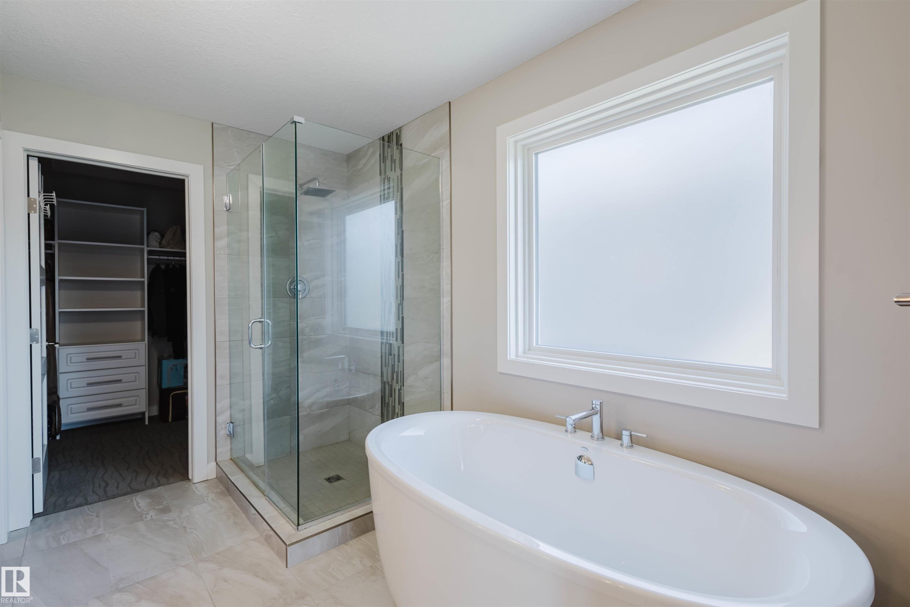 Freestanding soaking tub with chrome fixtures, a spacious glass-enclosed shower with a rainfall showerhead, and a tiled shower bench - 4125 Kennedy Green Sw, Edmonton, AB - Indoor Photo Showing Bathroom