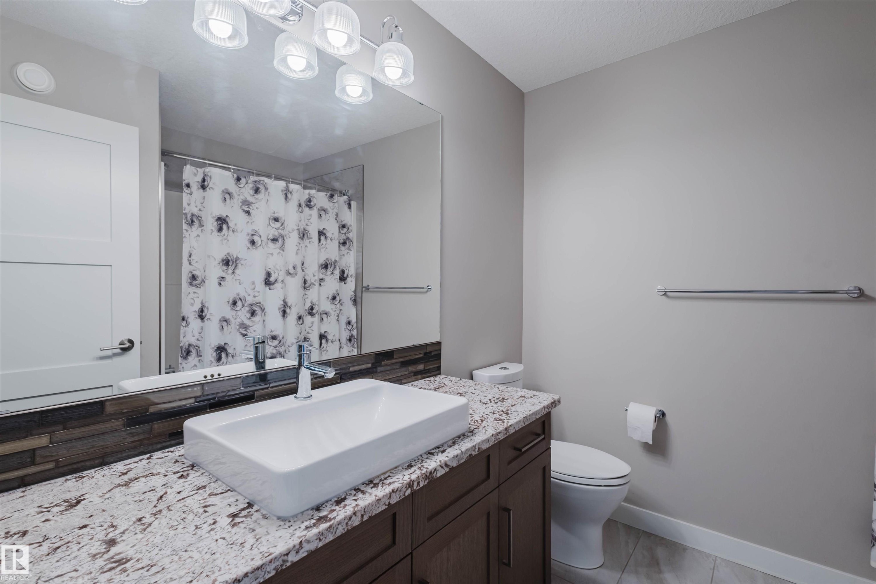 Bathroom vanity with a rectangular vessel sink, speckled countertop, dark wood-finish cabinetry, and a stacked stone-look backsplash - 4125 Kennedy Green Sw, Edmonton, AB - Indoor Photo Showing Bathroom