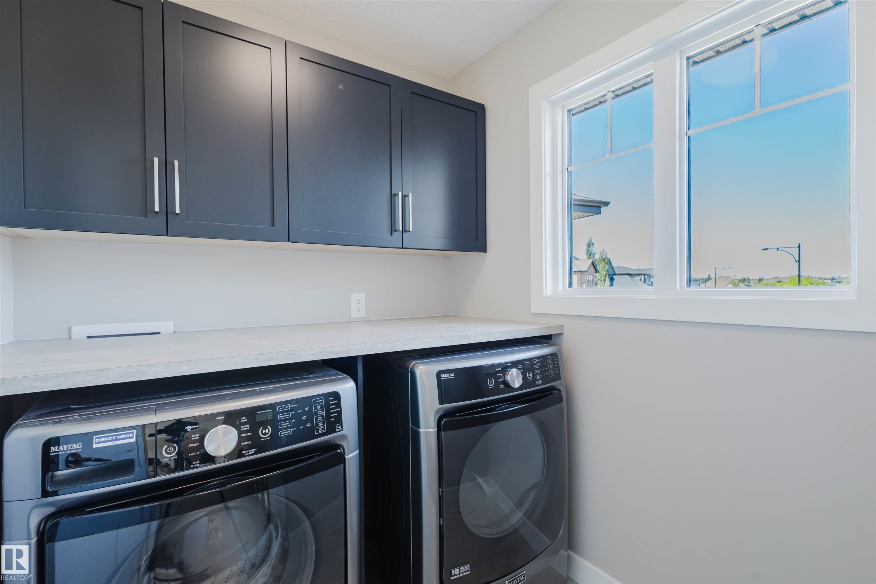 Laundry area featuring modern dark cabinetry, light-toned countertop, and bright window - 4125 Kennedy Green Sw, Edmonton, AB - Indoor Photo Showing Laundry Room