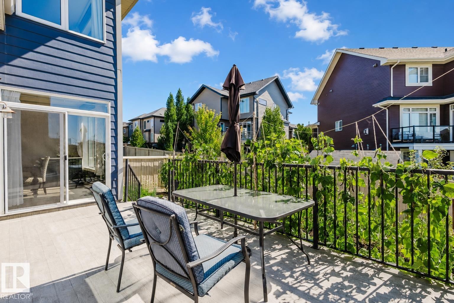 Spacious outdoor deck featuring light-toned decking, black metal railings, and vibrant green foliage - 4125 Kennedy Green Sw, Edmonton, AB - Outdoor With Deck Patio Veranda