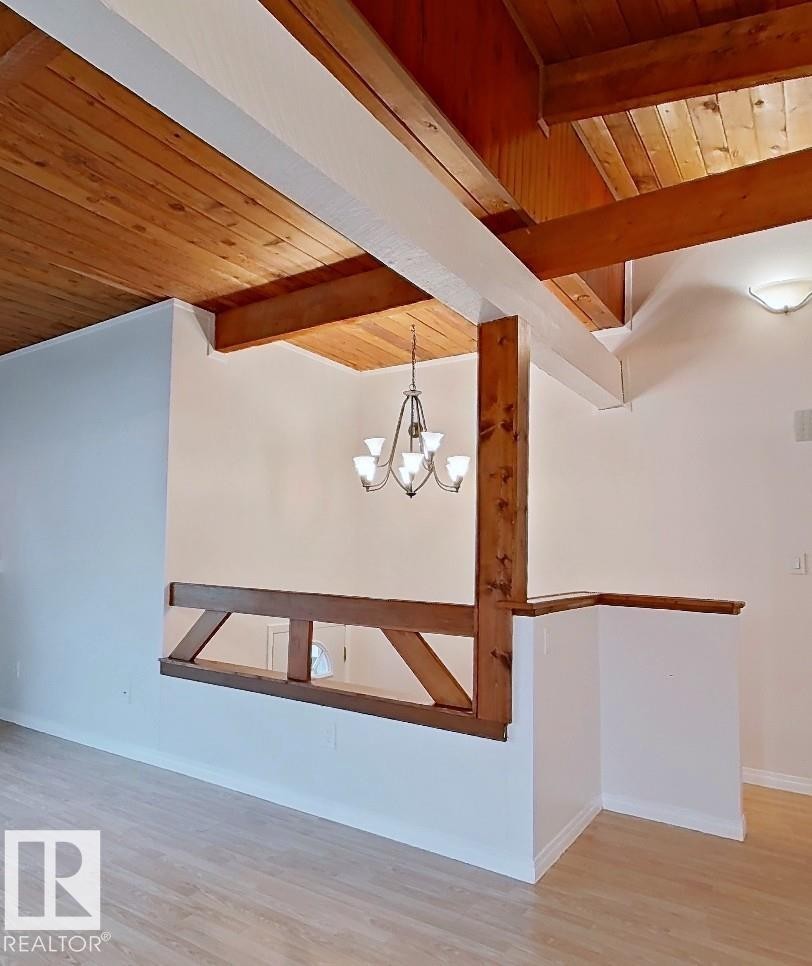 Vaulted wood-plank ceilings with exposed wood beams, a six-light chandelier, a decorative wood railing, and wood-finish flooring - 60 Northwoods Village Nw, Edmonton, AB - Indoor Photo Showing Other Room