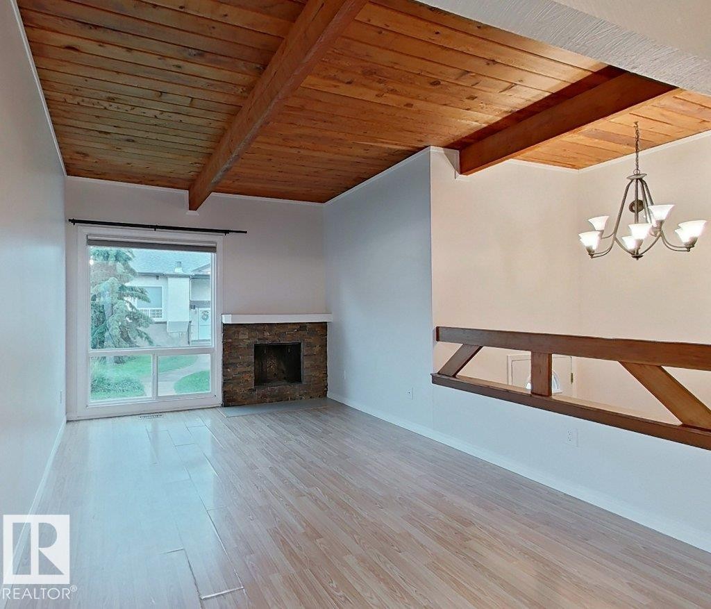 Spacious living area featuring wood-finish flooring, a stone-clad fireplace with a white mantel, and a large window providing outdoor views - 60 Northwoods Village Nw, Edmonton, AB - Indoor With Fireplace