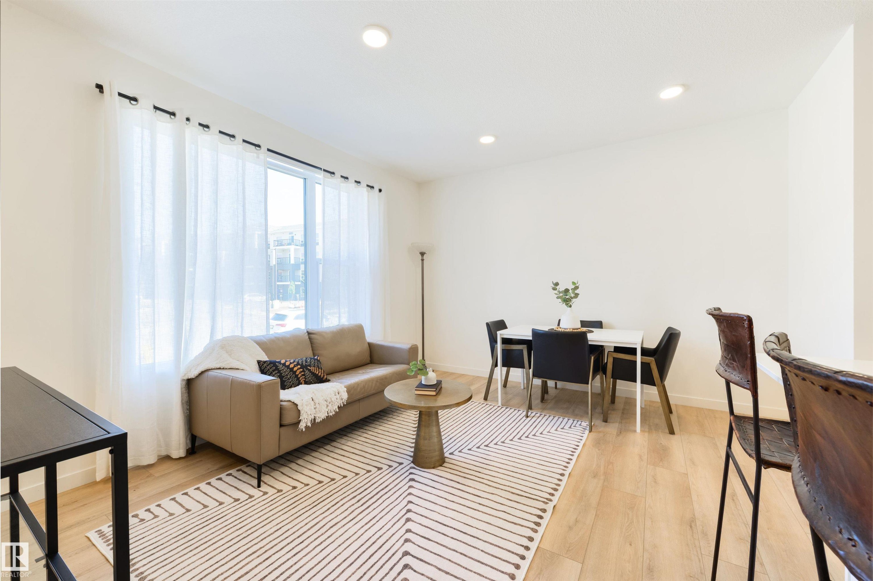 Open-concept living area with light wood-finish flooring, recessed lighting, and a large window with sheer white drapery - 323 Rankin Drive, St. Albert, AB - Indoor