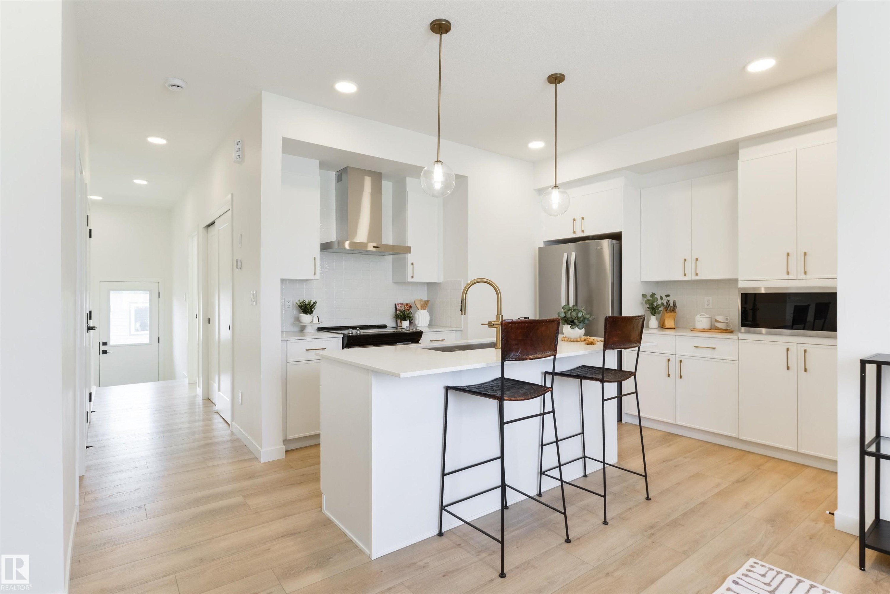 Modern kitchen featuring white cabinetry, a central island with a solid surface countertop, stainless steel appliances, and wood-finish flooring - 323 Rankin Drive, St. Albert, AB - Indoor Photo Showing Kitchen With Upgraded Kitchen