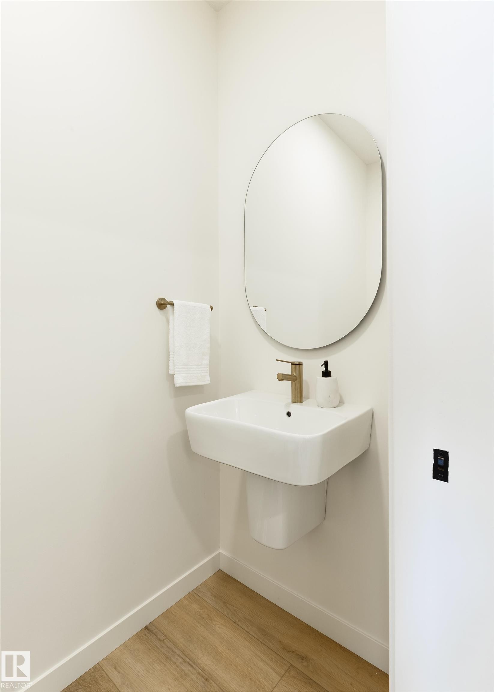 Bathroom with pedestal sink, elliptical mirror, and wood-finish flooring - 323 Rankin Drive, St. Albert, AB - Indoor Photo Showing Bathroom