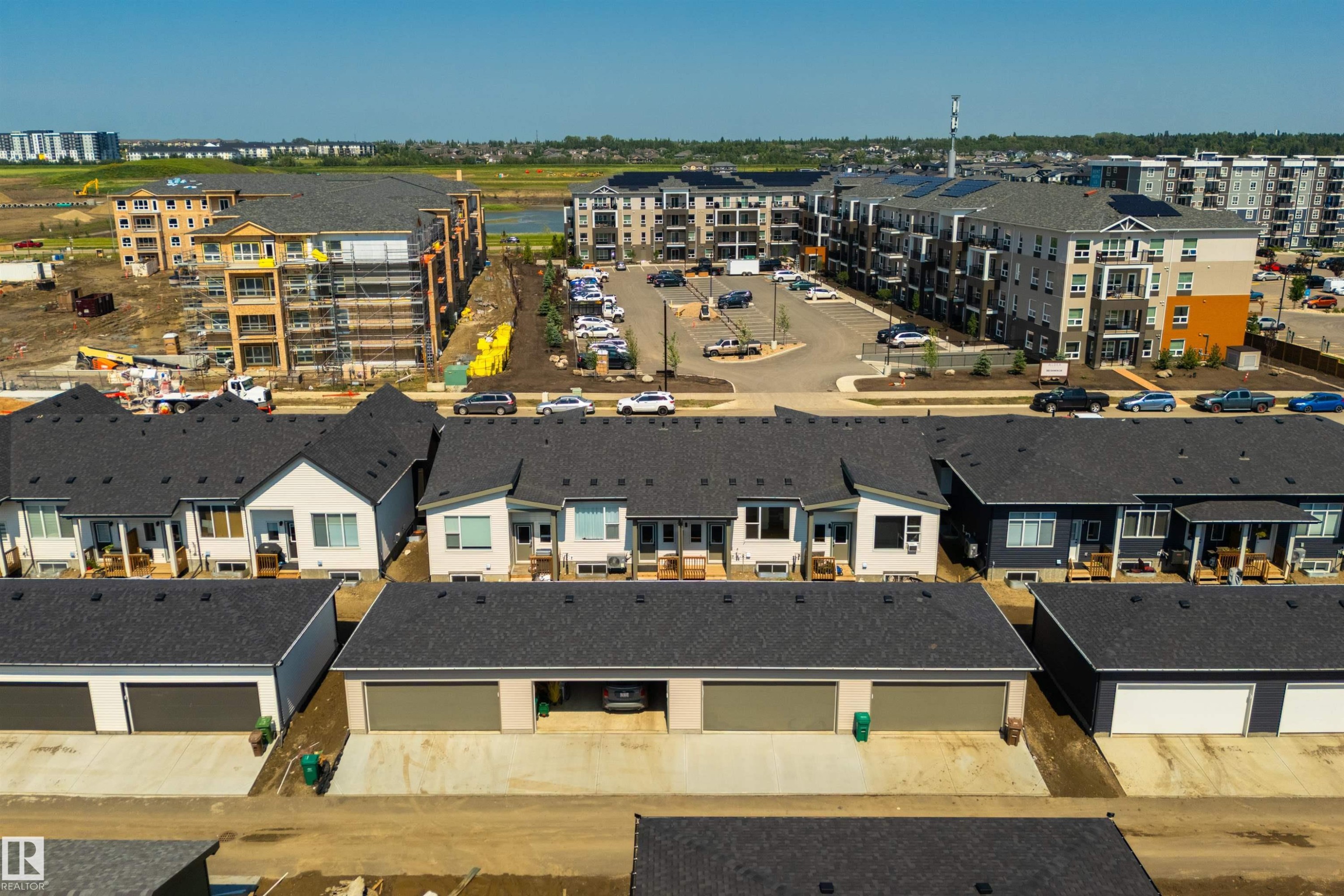 Aerial perspective showcasing multiple properties including detached garages with dark sectional doors, a row of townhouses with dark shingled roofs, and multi-story apartment buildings with balconies - 323 Rankin Drive, St. Albert, AB - Outdoor With View