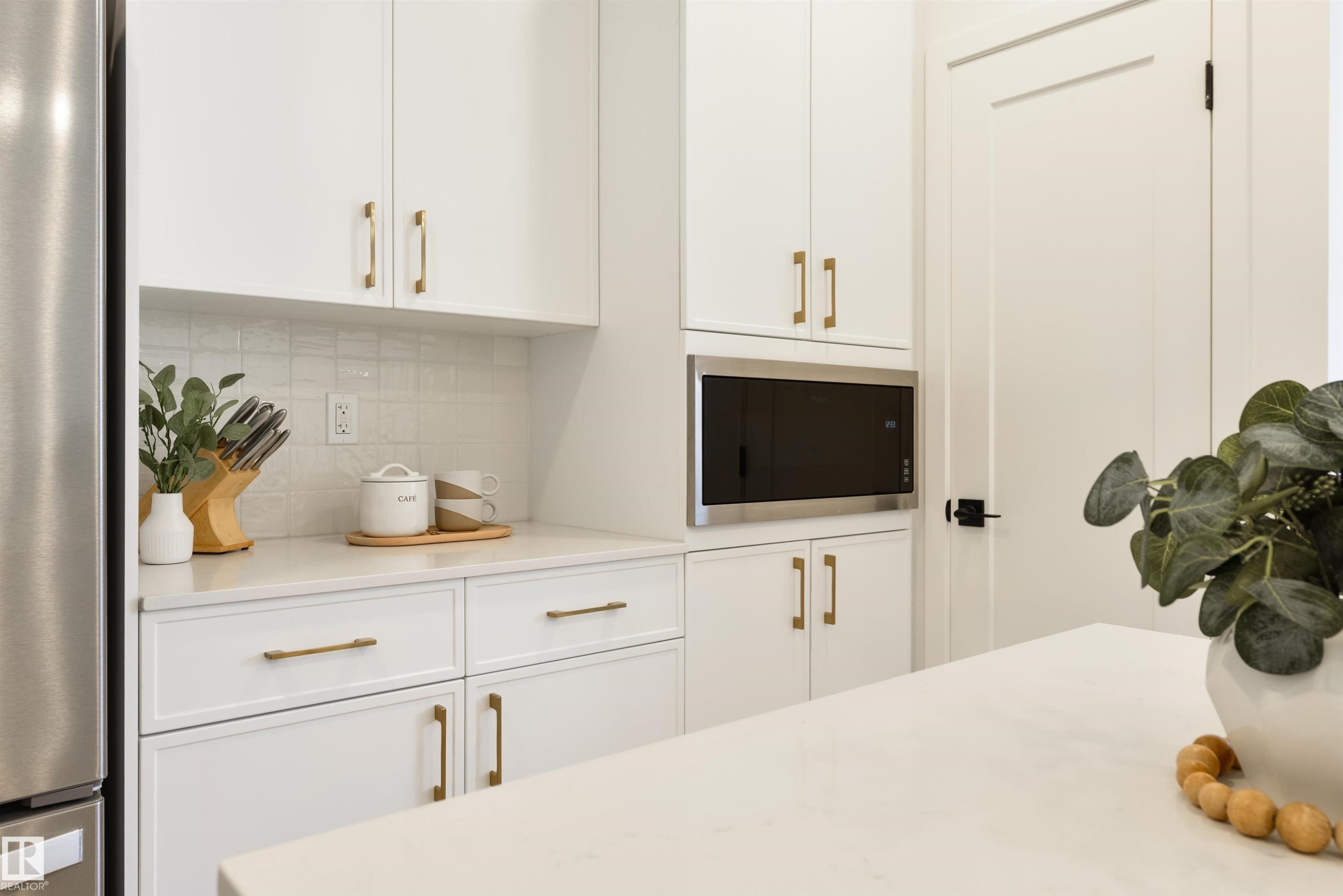 Modern kitchen featuring white cabinetry with gold-tone hardware, a stainless steel built-in microwave, and light-colored countertops - 323 Rankin Drive, St. Albert, AB - Indoor