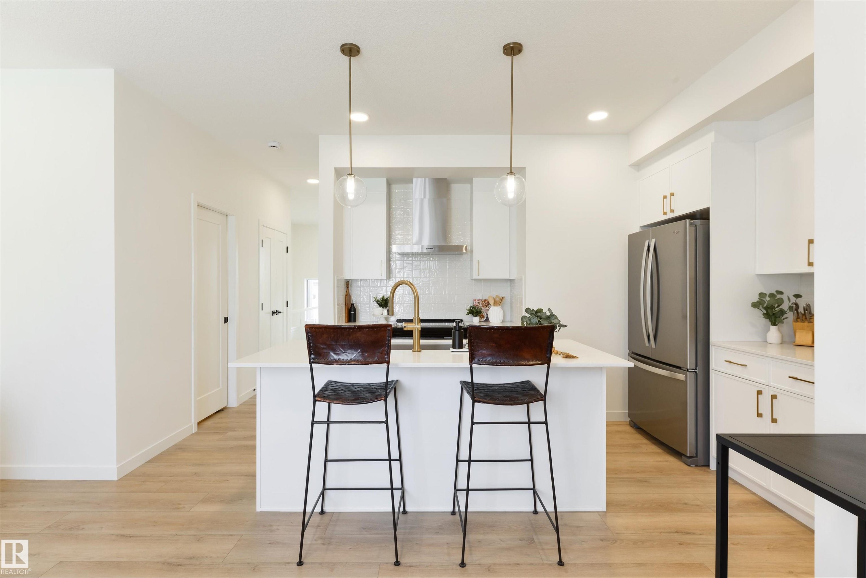 Contemporary kitchen featuring a white island, gold-tone hardware, stainless steel appliances, a tile backsplash, and light wood-finish flooring - 323 Rankin Drive, St. Albert, AB - Indoor Photo Showing Kitchen With Upgraded Kitchen