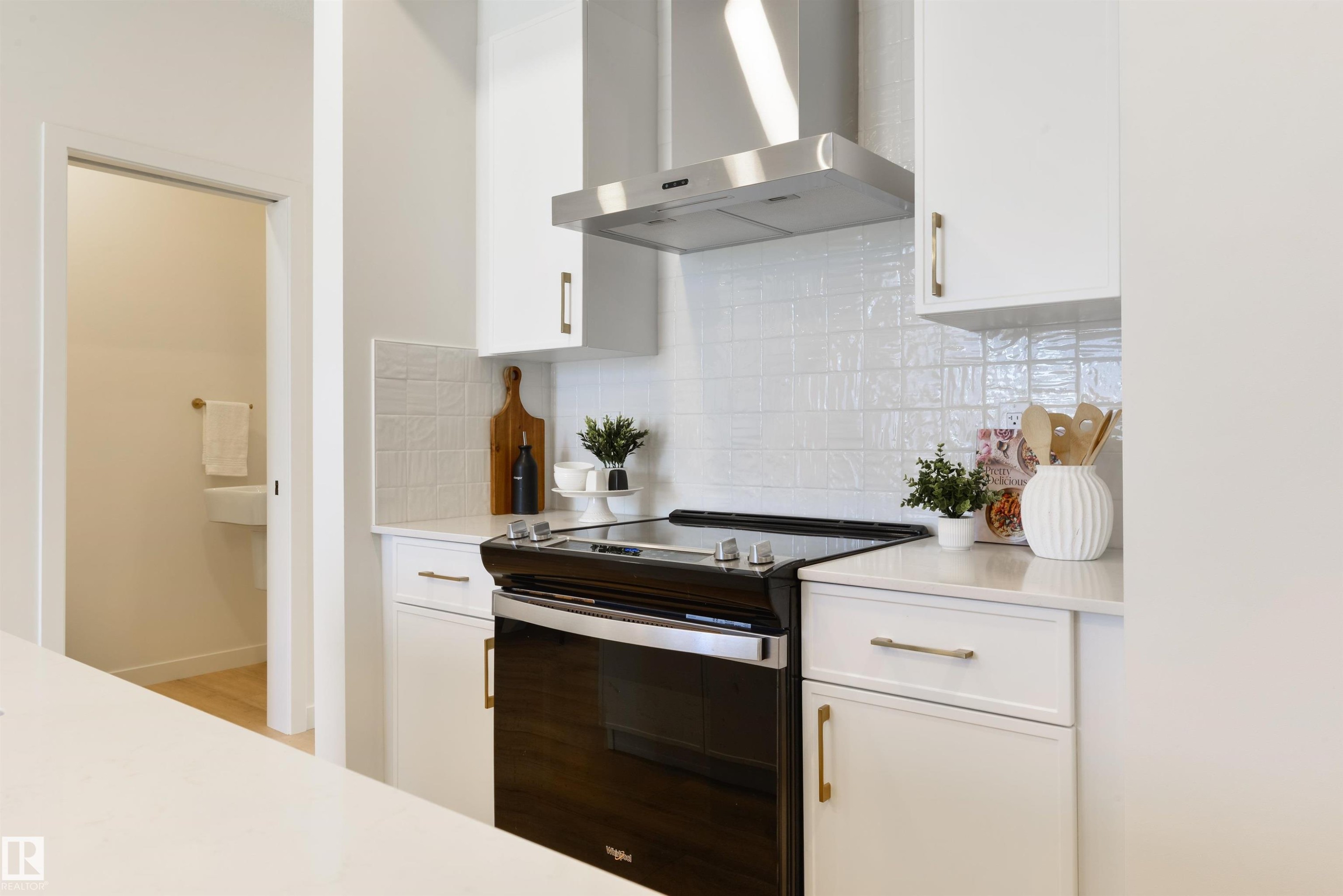 Modern kitchen featuring a black oven with a stainless steel range hood, white cabinetry, and white textured tile backsplash - 323 Rankin Drive, St. Albert, AB - Indoor Photo Showing Kitchen