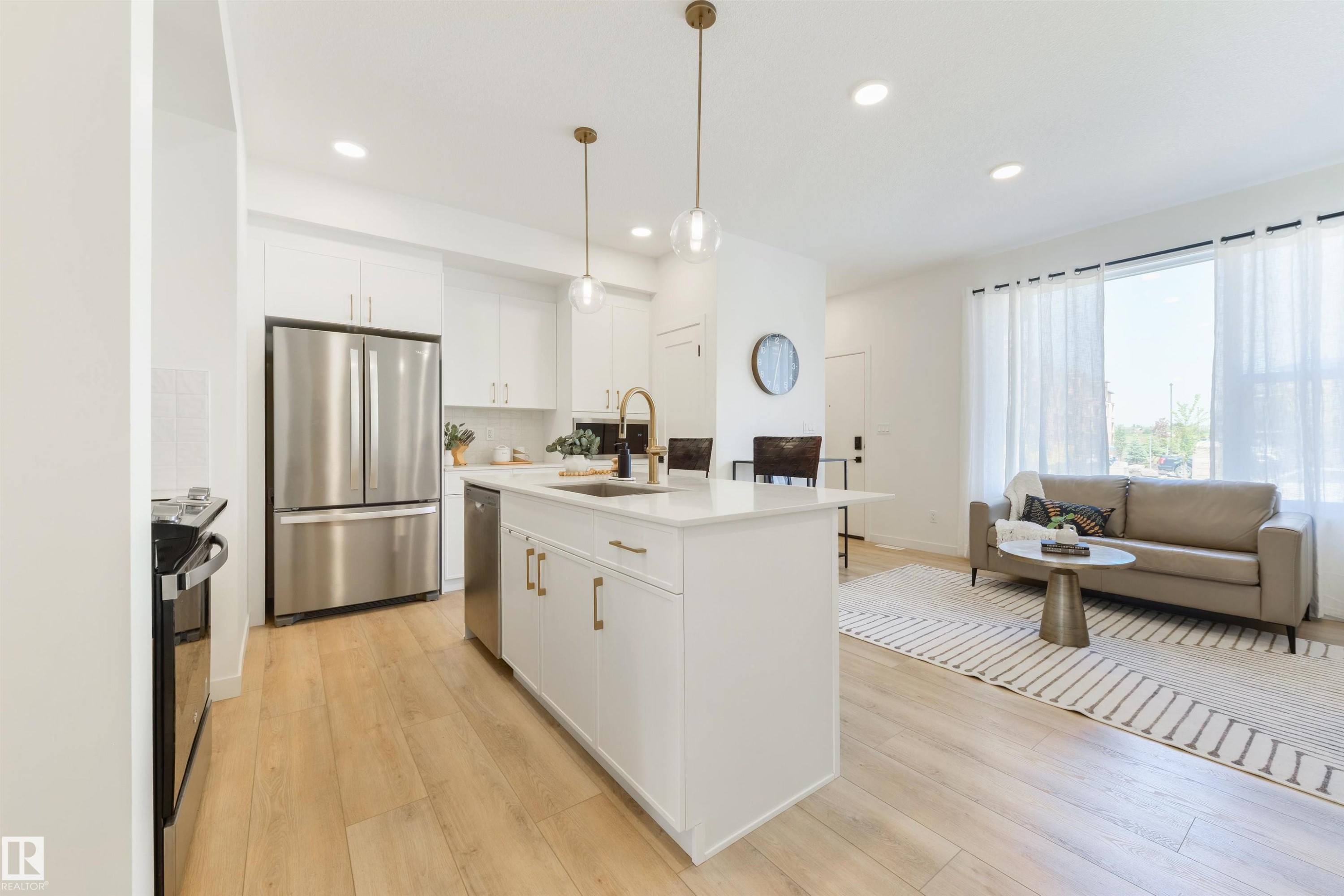 Open-concept living space featuring a kitchen island with pendant lighting, stainless steel appliances, light wood-finish flooring, recessed lighting, and a large window with sheer curtains - 323 Rankin Drive, St. Albert, AB - Indoor Photo Showing Kitchen