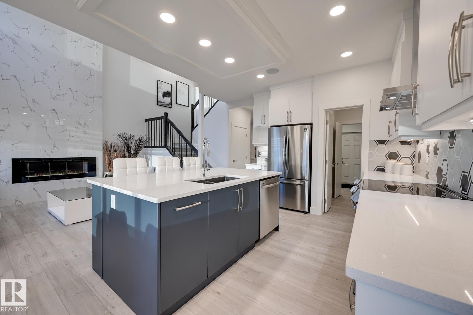 Open-concept kitchen featuring a large island with seating, stainless steel appliances, white cabinetry, and a modern hexagonal tile backsplash - 1776 Crossbill Loop Nw, Edmonton, AB - Indoor Photo Showing Kitchen With Double Sink With Upgraded Kitchen