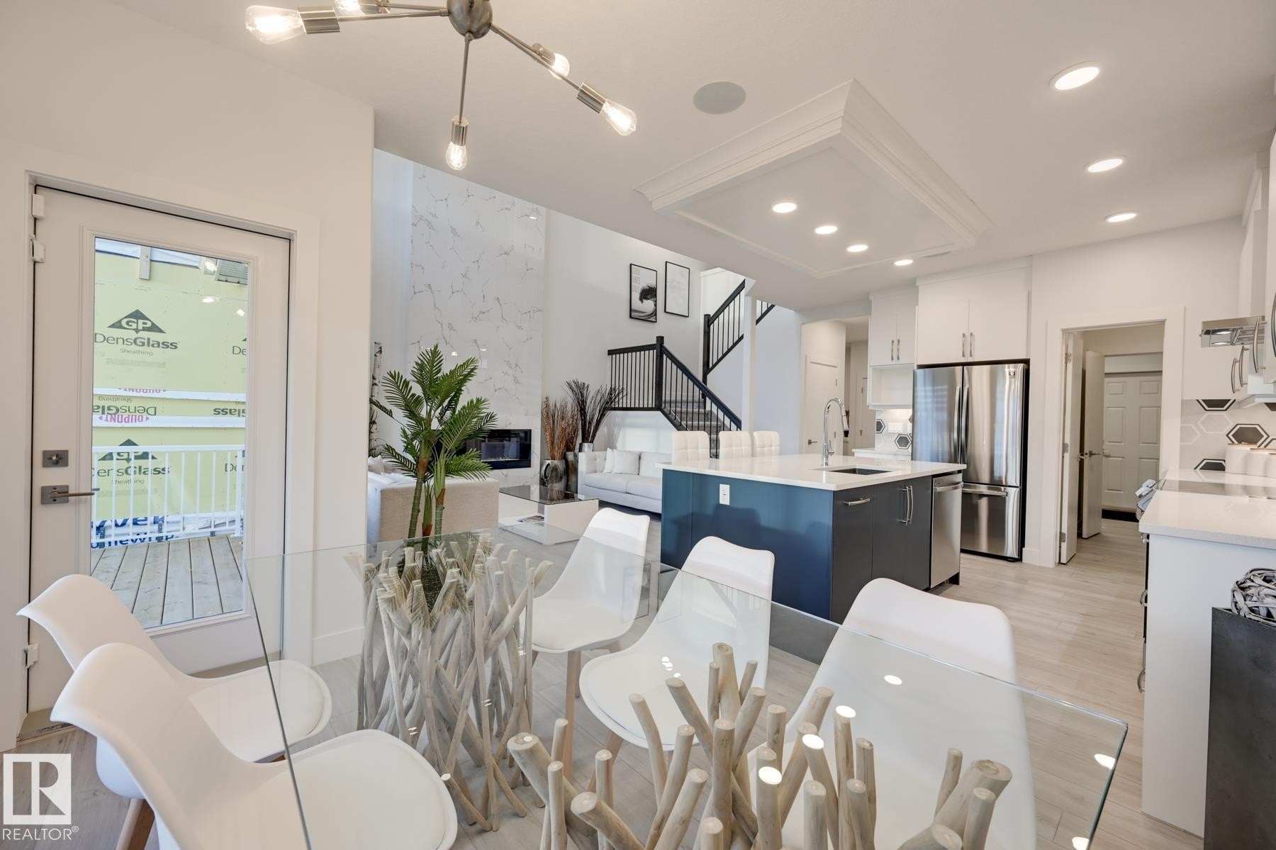 Open-concept living area with light wood-finish flooring, a contemporary kitchen island, stainless steel appliances, and a modern chandelier - 1776 Crossbill Loop Nw, Edmonton, AB - Indoor