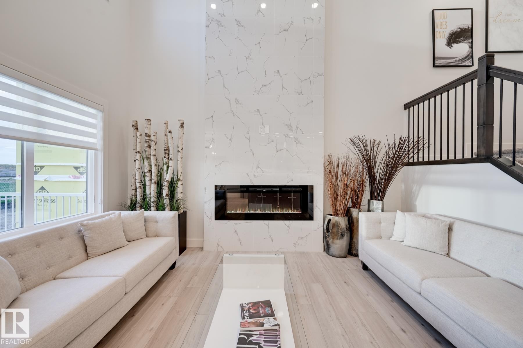 Vaulted ceiling living area featuring a full-height fireplace with stone-finish surround, light wood-finish flooring, and a staircase with dark wood-finish handrail and black balusters - 1776 Crossbill Loop Nw, Edmonton, AB - Indoor Photo Showing Living Room With Fireplace