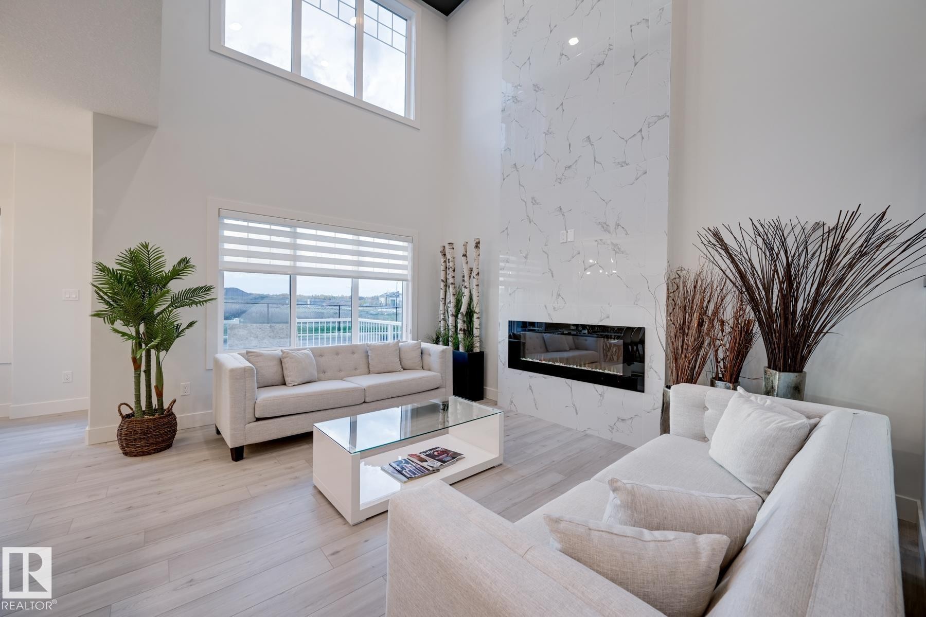 Spacious living area featuring a floor-to-ceiling fireplace with a marble-look surround, a linear electric fireplace insert, and high ceilings - 1776 Crossbill Loop Nw, Edmonton, AB - Indoor Photo Showing Living Room With Fireplace
