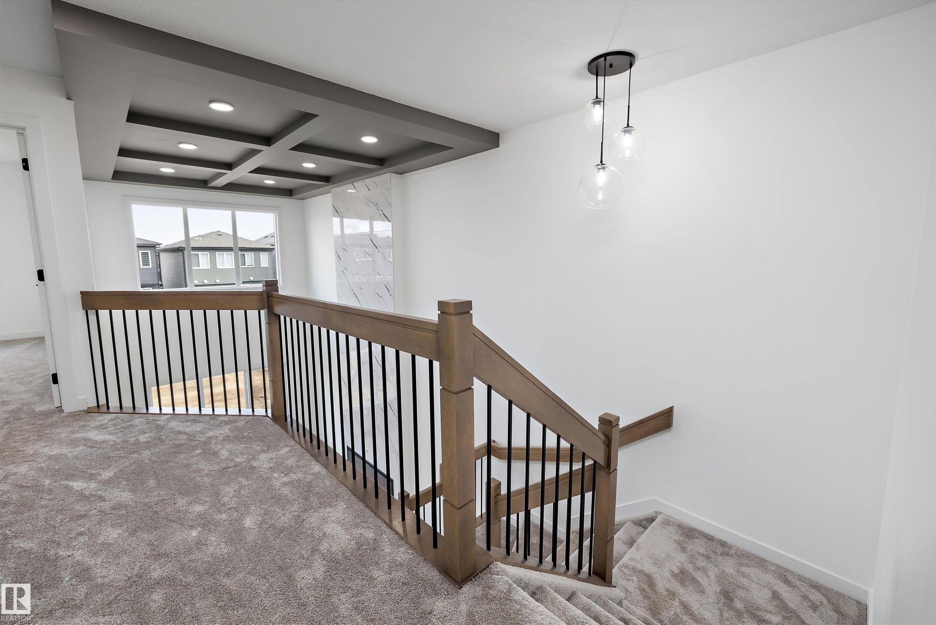 Spacious upper-level landing featuring custom wood-finish railings with metal balusters, recessed ceiling with integrated coffers and pendant lighting, carpet flooring, and abundant natural light from multi-pane windows - 1776 Crossbill Loop Nw, Edmonton, AB