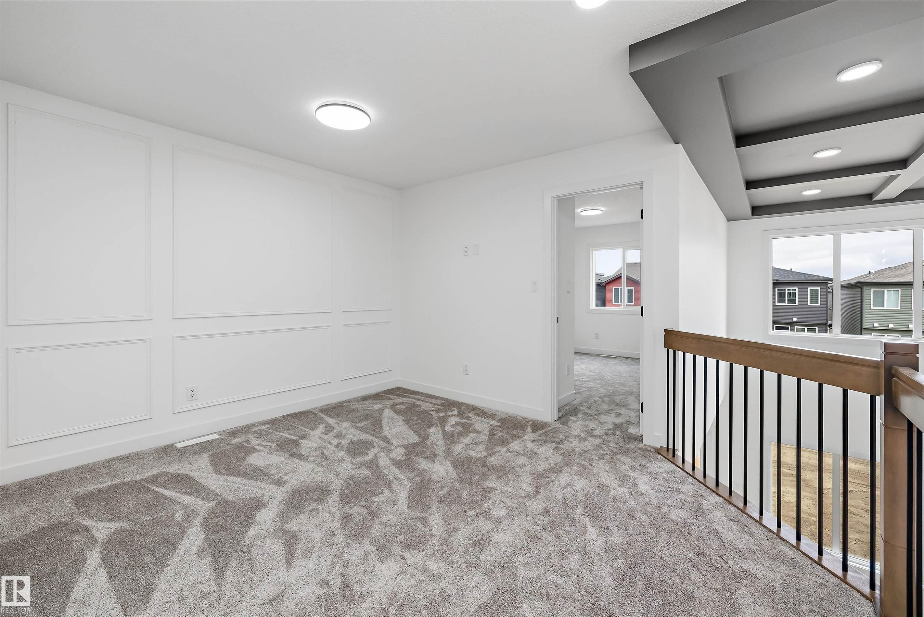 Panel molding accent wall, recessed lighting, neutral tone carpeting, coffered ceiling detail, and wood-finish handrailing with black iron spindles - 1776 Crossbill Loop Nw, Edmonton, AB