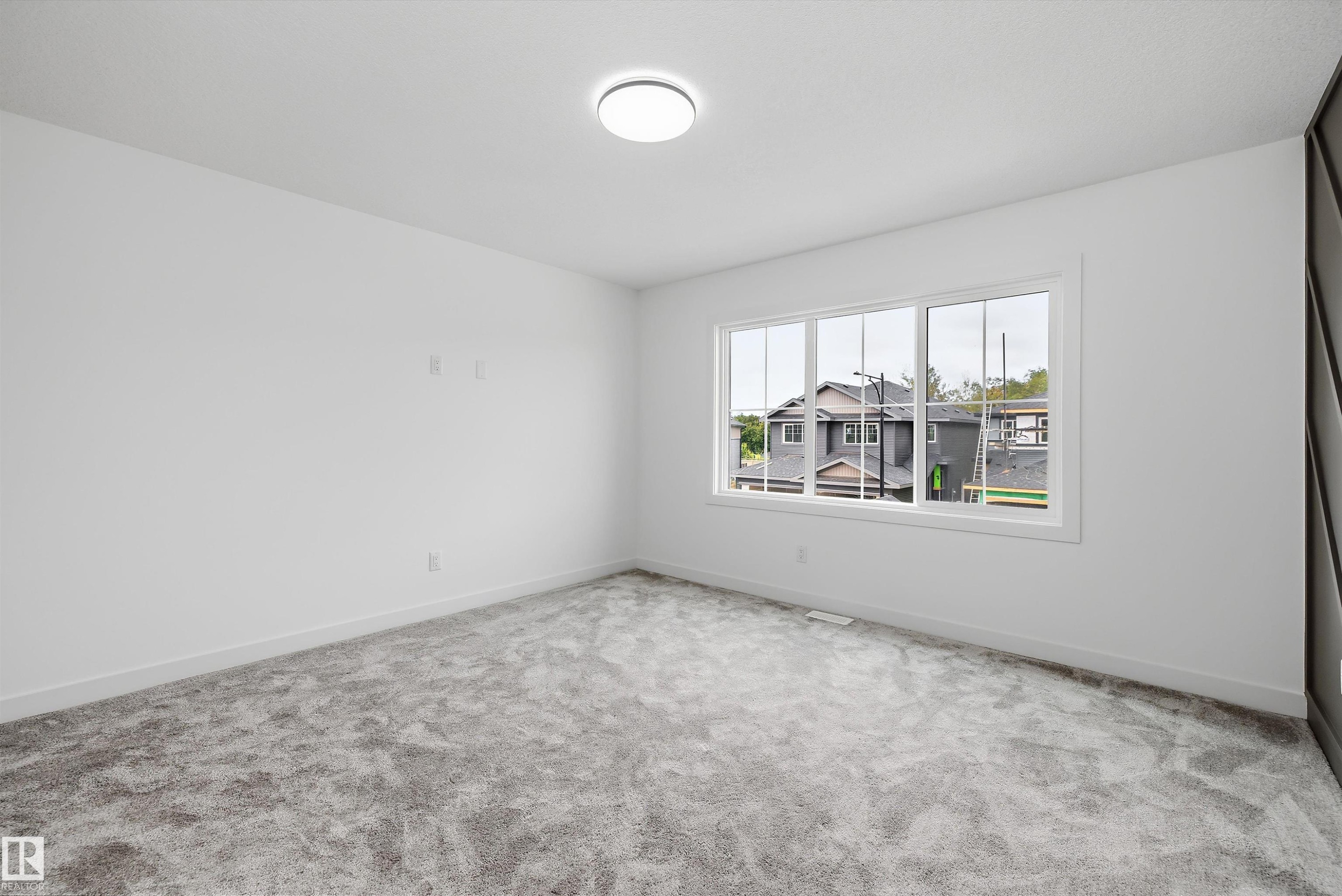 Bright secondary bedroom featuring neutral wall finishes, plush carpeting, and a large multi-pane window with natural light and exterior visibility - 1776 Crossbill Loop Nw, Edmonton, AB