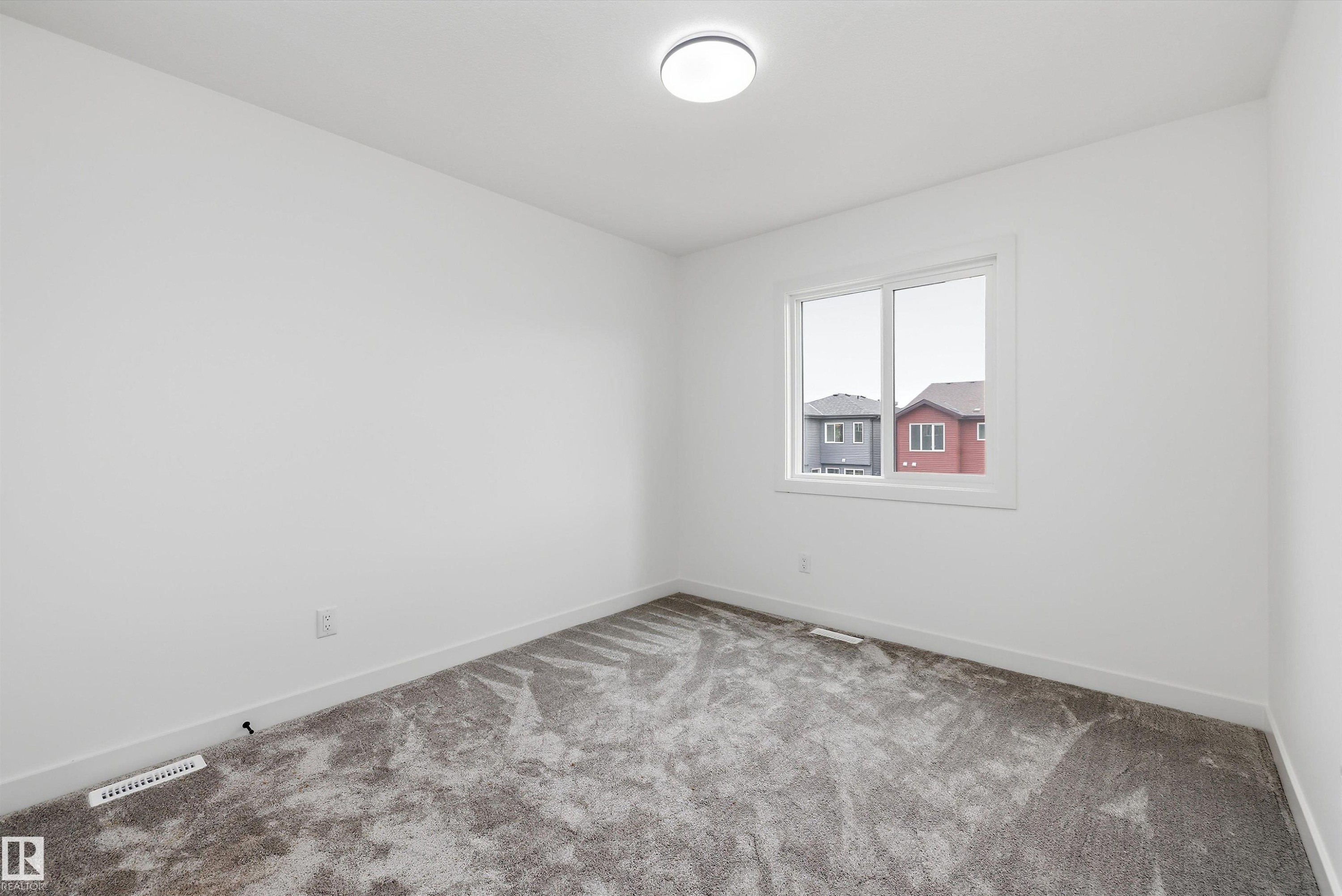 Bright secondary bedroom featuring recessed ceiling lighting, carpet flooring, and a large window with natural light and neighborhood views - 1776 Crossbill Loop Nw, Edmonton, AB