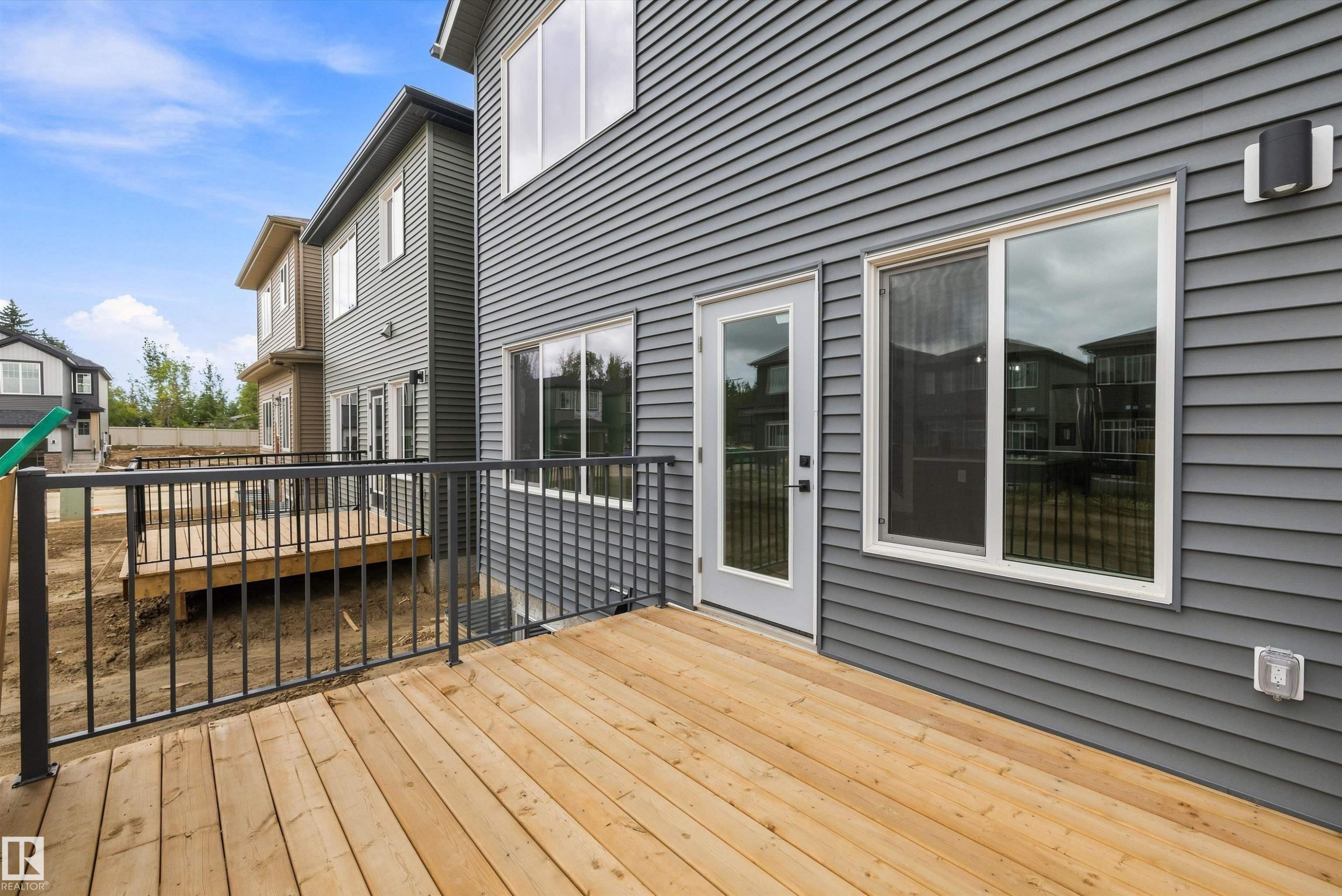Expansive wood deck with black metal railings, gray horizontal siding, and large windows - 1776 Crossbill Loop Nw, Edmonton, AB