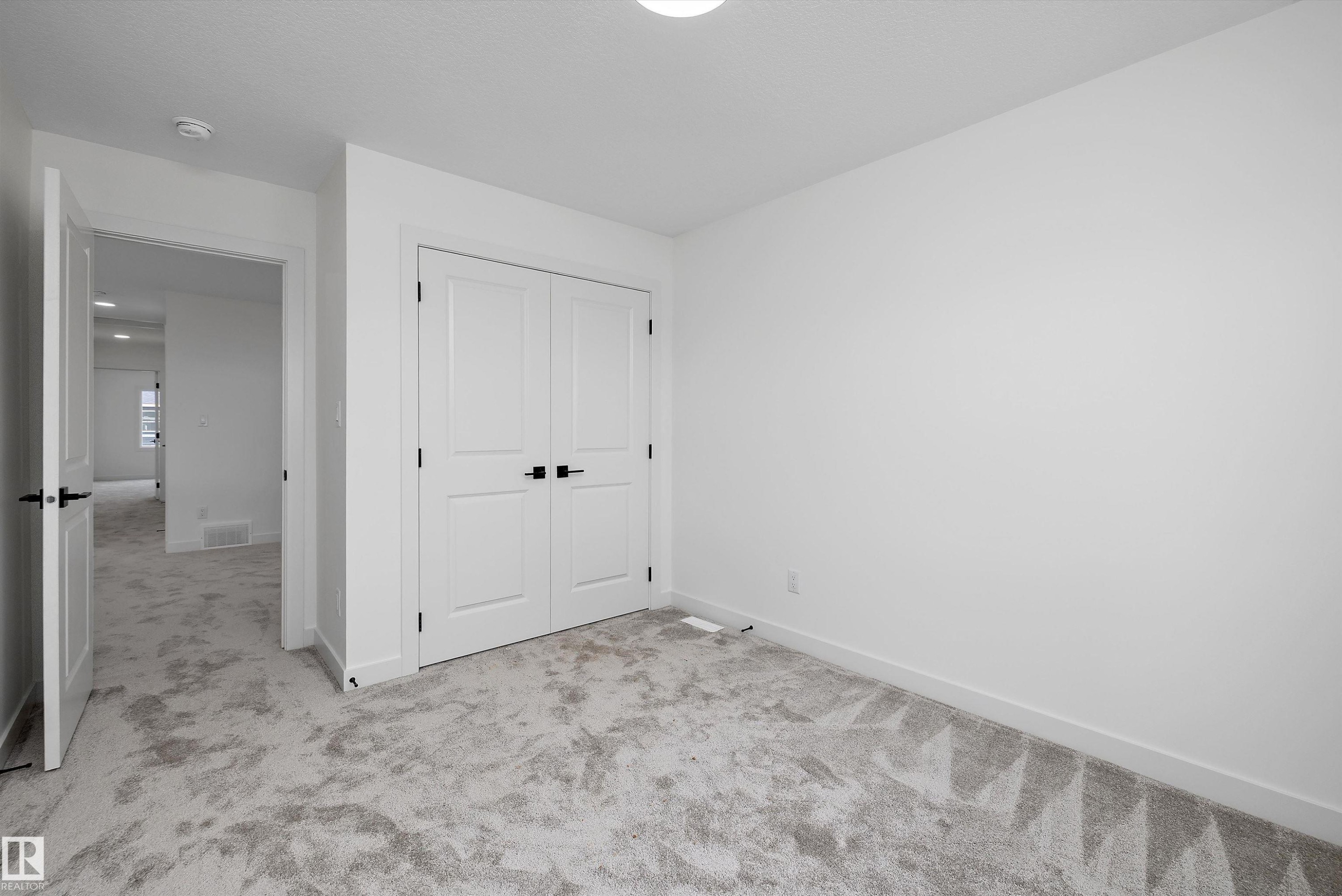 Plush carpet flooring, white painted walls, white paneled bifold closet doors, and matte black hardware - 1776 Crossbill Loop Nw, Edmonton, AB