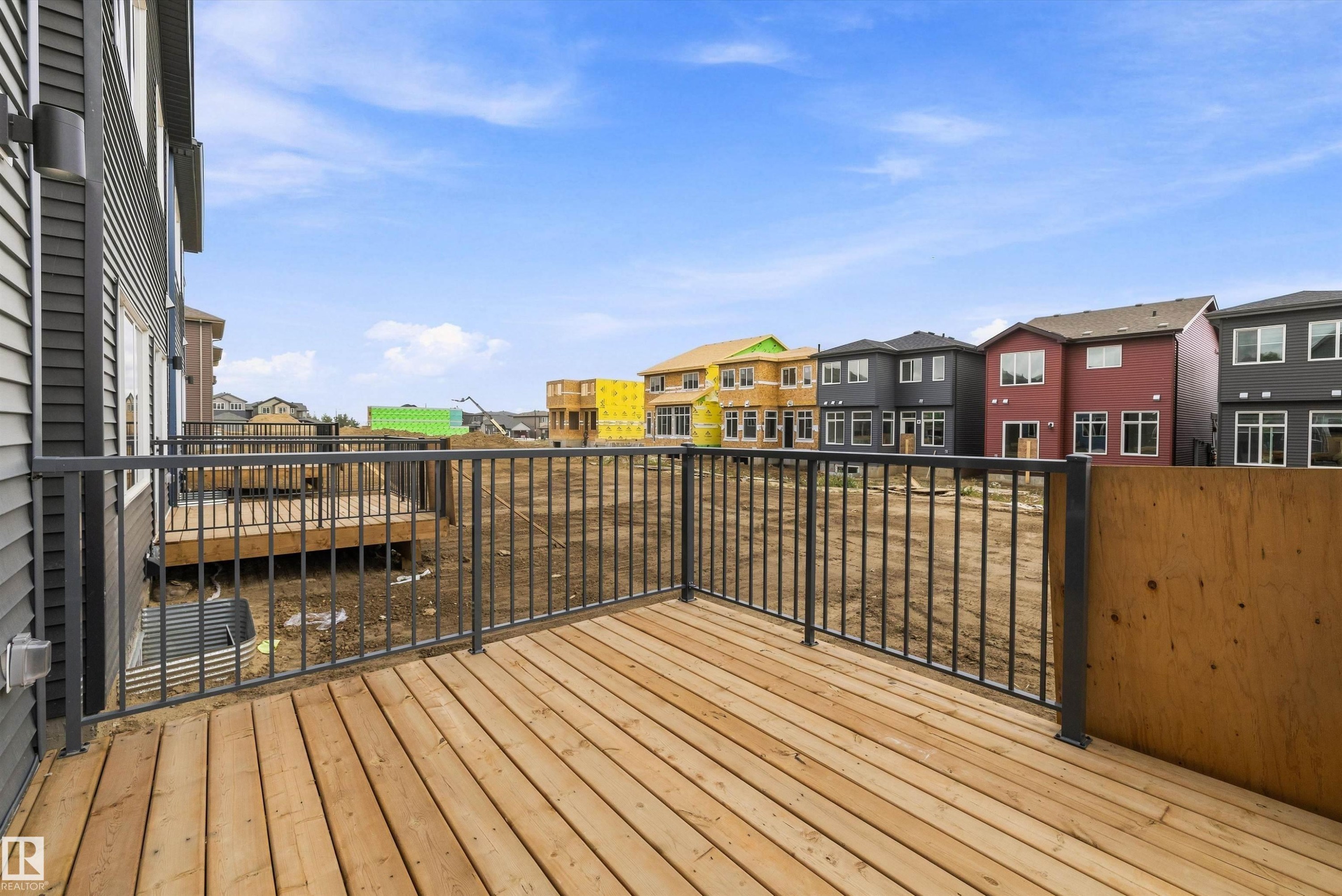 Spacious composite deck featuring warm wood-finish flooring and black metal railing, overlooking a vibrant neighborhood streetscape with colorful residential architecture - 1776 Crossbill Loop Nw, Edmonton, AB