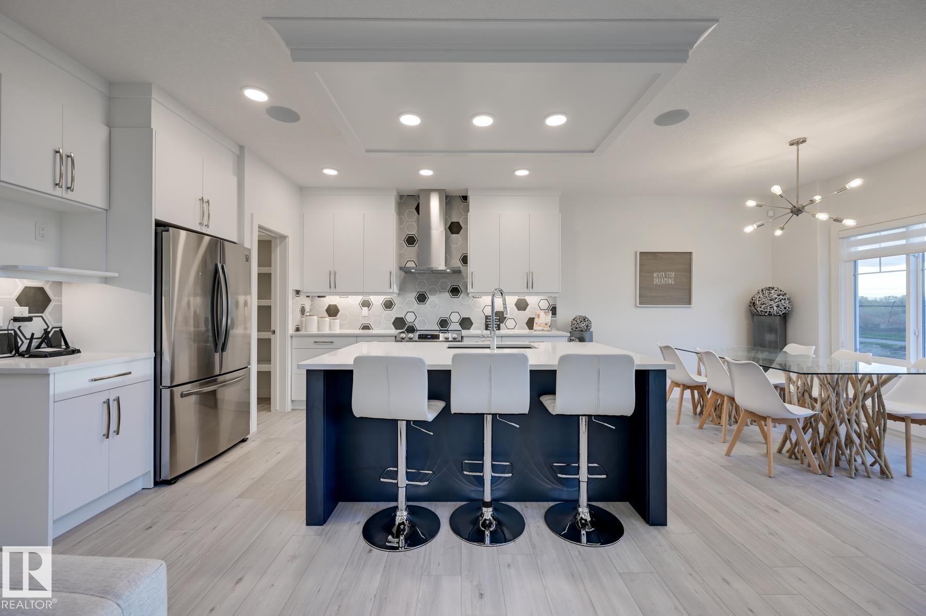 Open-concept kitchen featuring an oversized island with seating, integrated stainless steel appliances, contemporary hexagon tile backsplash, recessed lighting, and wood-finish flooring - 1776 Crossbill Loop Nw, Edmonton, AB - Indoor