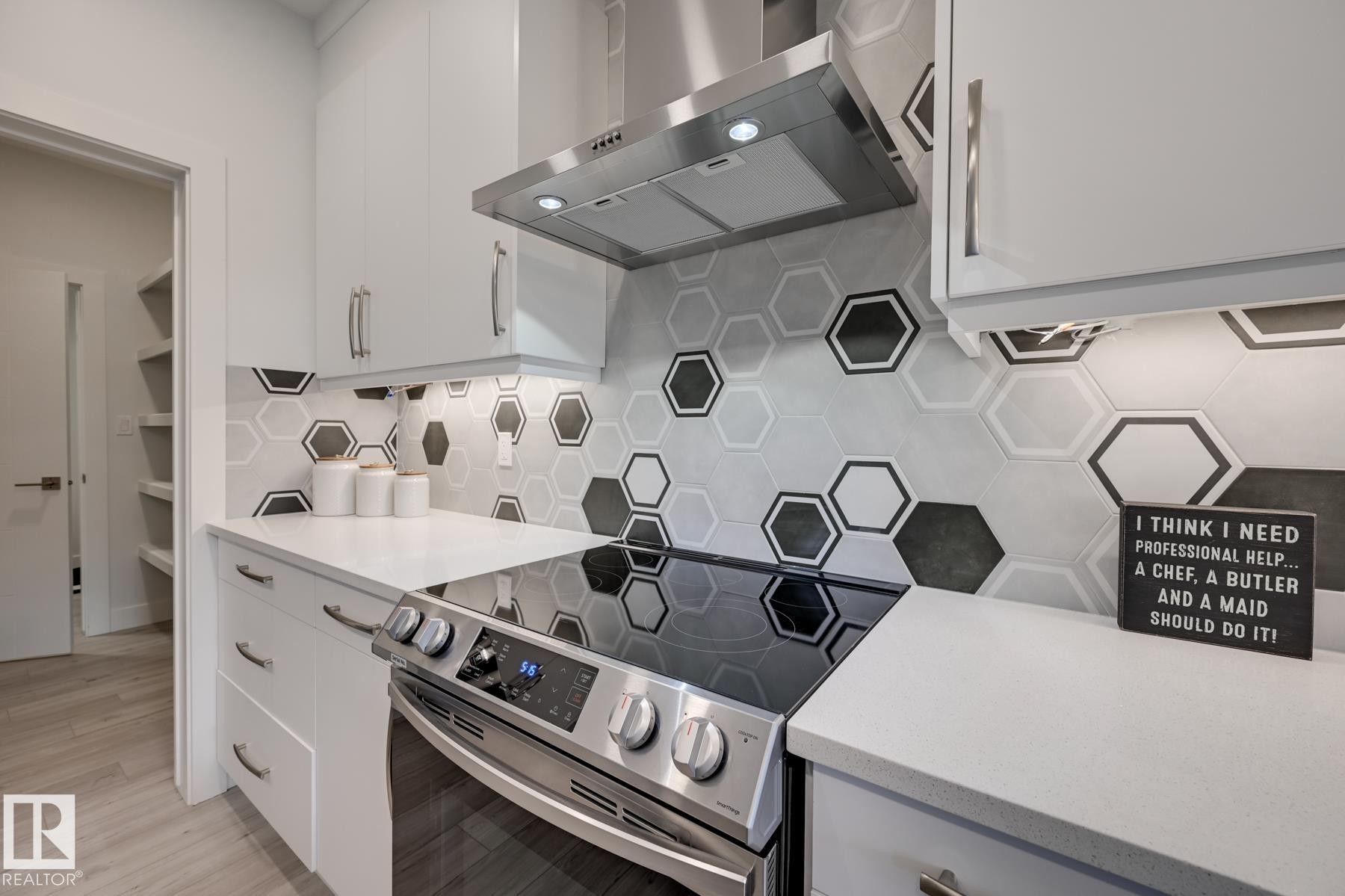 Contemporary kitchen featuring an electric range, stainless steel vent hood, and a unique hexagonal tile backsplash - 1776 Crossbill Loop Nw, Edmonton, AB - Indoor Photo Showing Kitchen