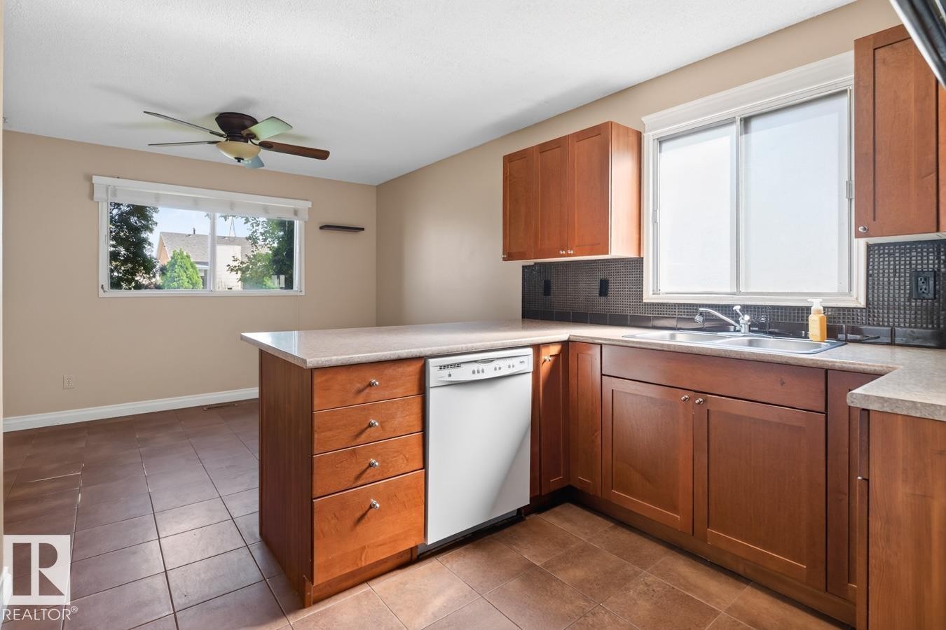 Kitchen featuring a peninsula with countertop seating, wood-finish cabinetry, and a tile backsplash - 4003 41 Avenue Nw, Edmonton, AB - Indoor Photo Showing Kitchen With Double Sink