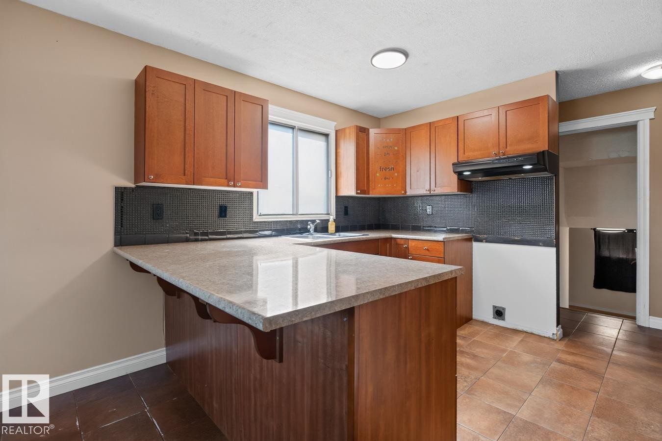 Kitchen featuring wood cabinetry, light-toned countertops, a dark tiled backsplash, and recessed lighting - 4003 41 Avenue Nw, Edmonton, AB - Indoor Photo Showing Kitchen