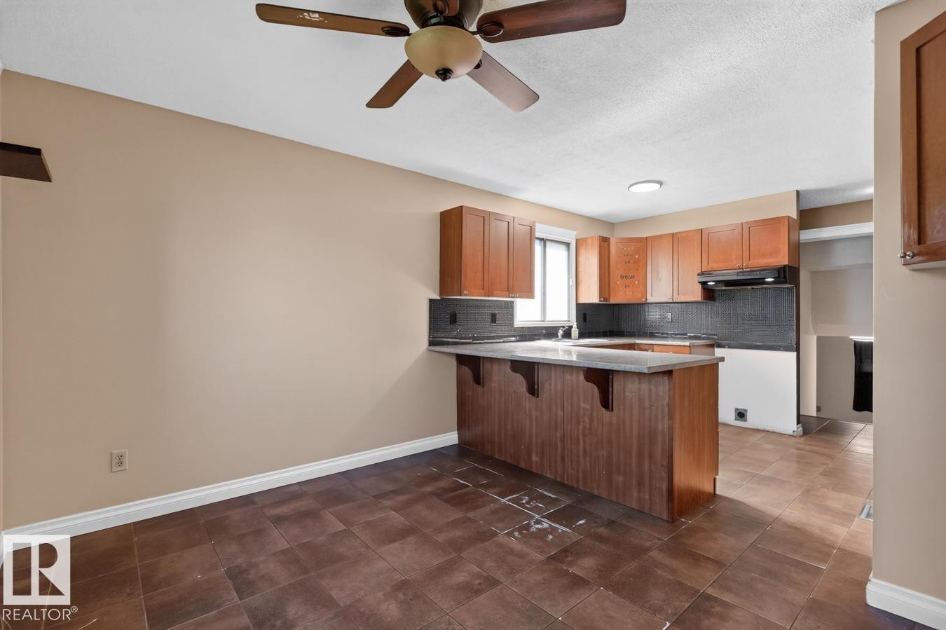Kitchen featuring wood cabinetry, dark countertops, and a breakfast bar with a support panel - 4003 41 Avenue Nw, Edmonton, AB - Indoor Photo Showing Kitchen
