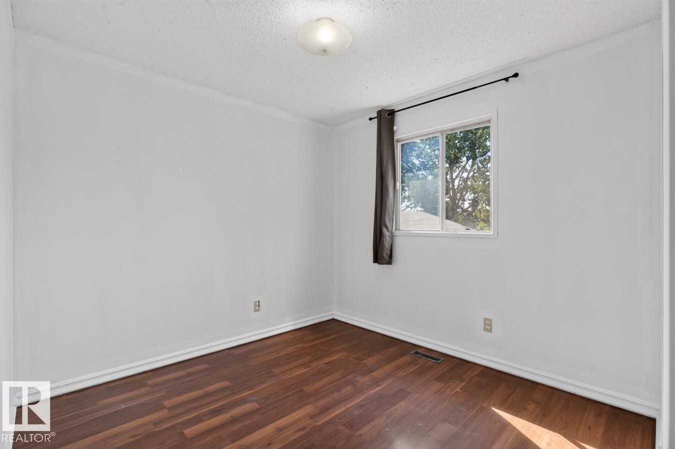 Room featuring wood-finish flooring, white baseboards, a white ceiling with a flush-mount light fixture, and a window with a dark curtain rod - 4003 41 Avenue Nw, Edmonton, AB - Indoor Photo Showing Other Room