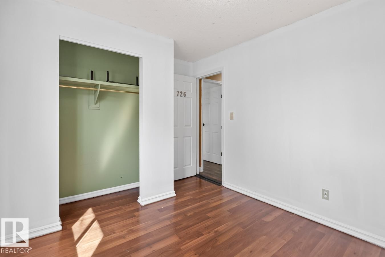 Room featuring wood-finish flooring, white baseboards, and a built-in closet with a hanging rod and shelving - 4003 41 Avenue Nw, Edmonton, AB - Indoor Photo Showing Other Room