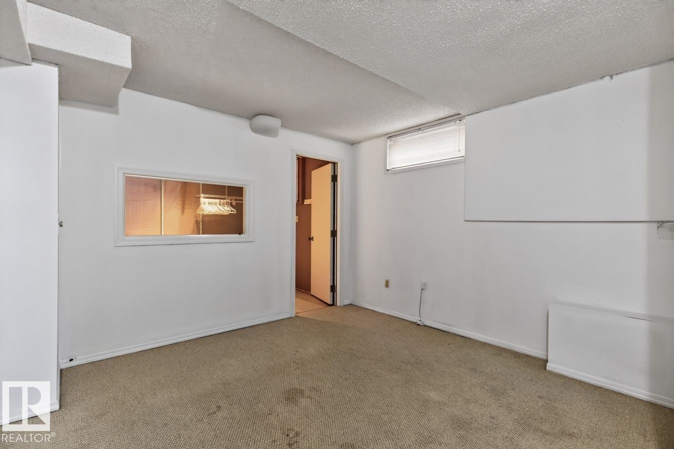 White walls with wall-to-wall carpeting, a small transom window, and a pass-through window with interior lighting - 4003 41 Avenue Nw, Edmonton, AB - Indoor Photo Showing Other Room