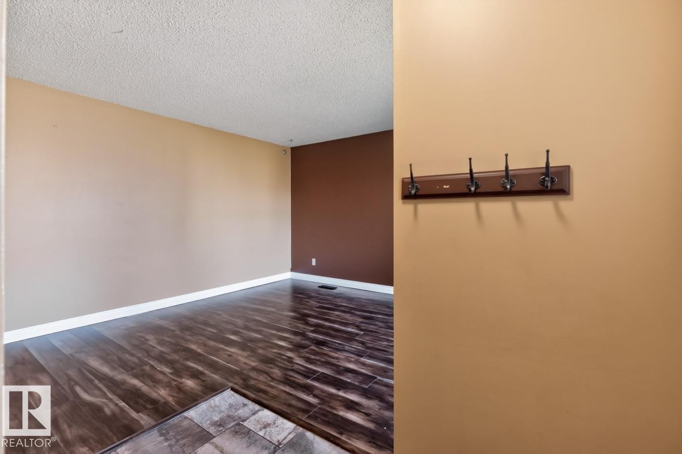 Spacious room featuring wood-finish flooring, light beige and accent brown wall paint, white baseboards, and a textured ceiling - 4003 41 Avenue Nw, Edmonton, AB - Indoor Photo Showing Other Room
