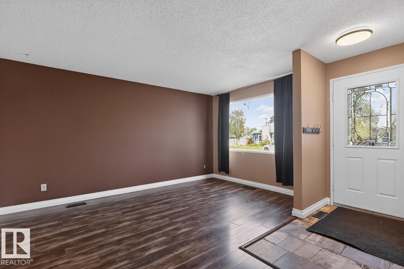 Spacious living area featuring wood-finish flooring, a large picture window, and a white entry door with decorative glass inserts - 4003 41 Avenue Nw, Edmonton, AB - Indoor Photo Showing Other Room