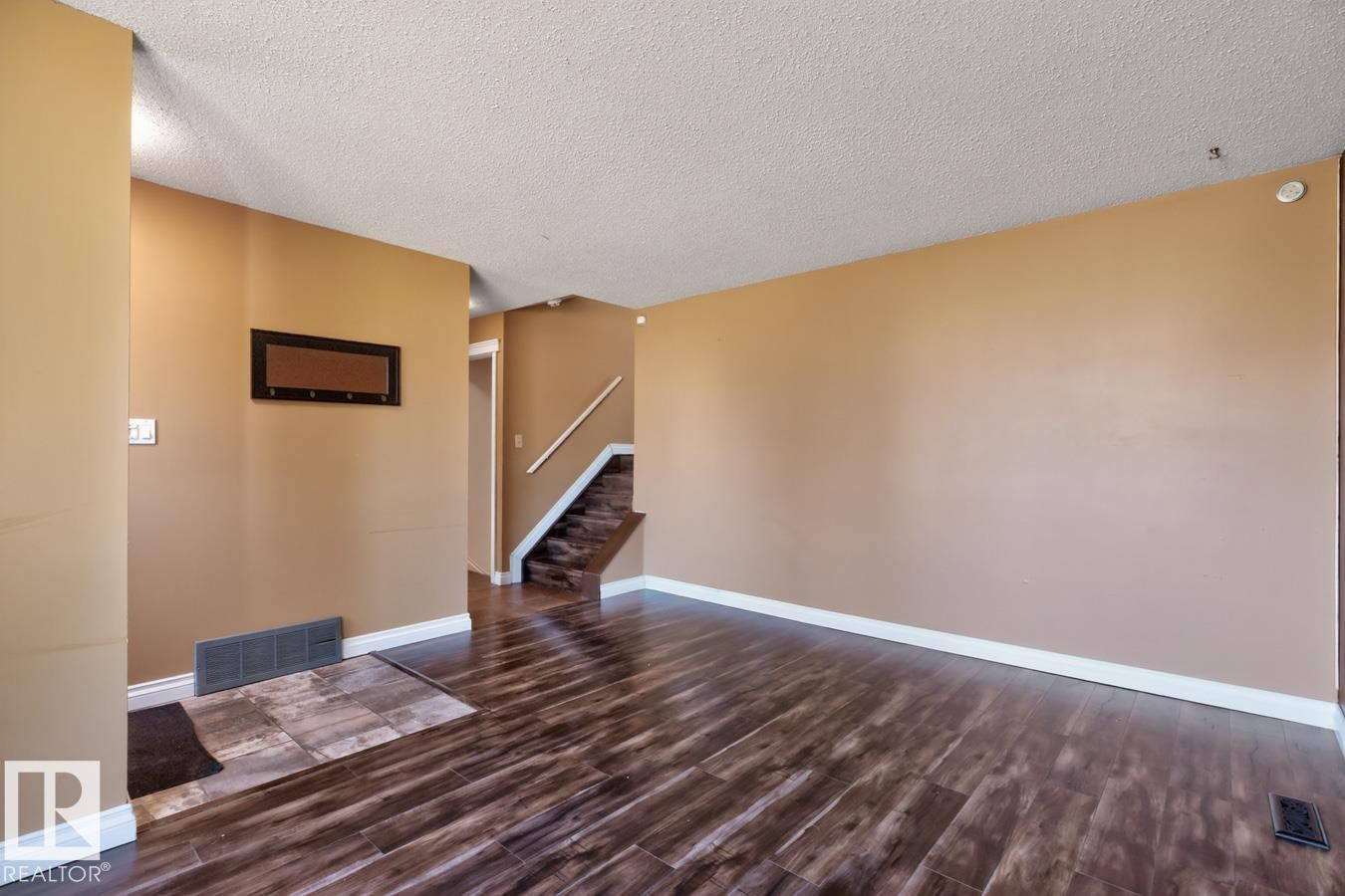 Spacious room featuring wood-finish flooring, light tan wall paint, and white baseboards - 4003 41 Avenue Nw, Edmonton, AB - Indoor Photo Showing Other Room