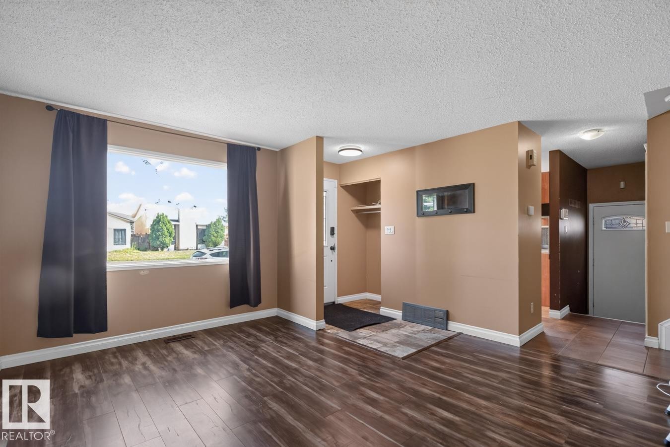 Spacious living area featuring wood-finish flooring, a large window, and light tan walls - 4003 41 Avenue Nw, Edmonton, AB - Indoor Photo Showing Other Room