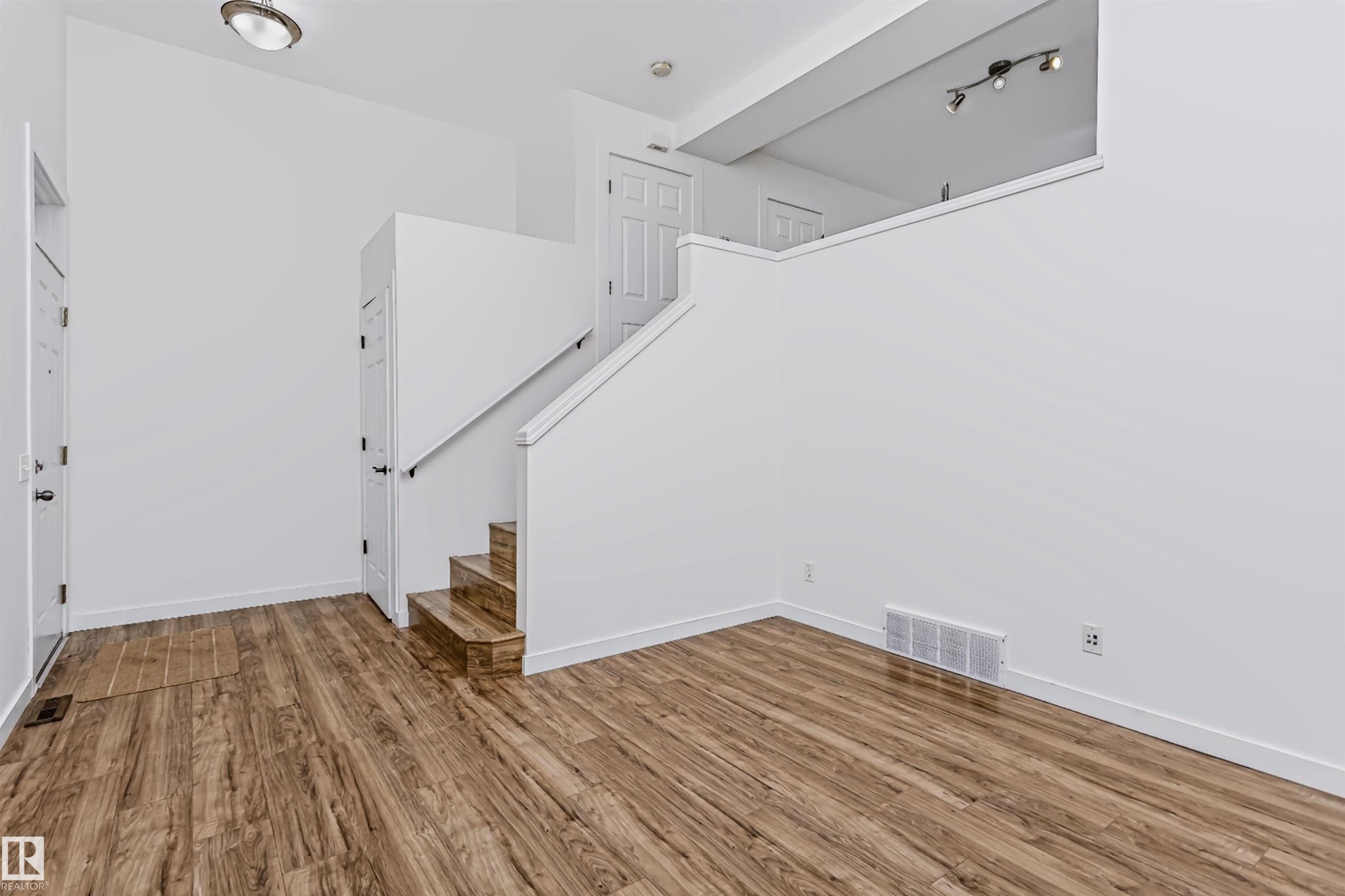 Open living space featuring wood-finish flooring, white walls, and a staircase with a white railing - #66 8304 11 Av Sw, Edmonton, AB - Indoor Photo Showing Other Room