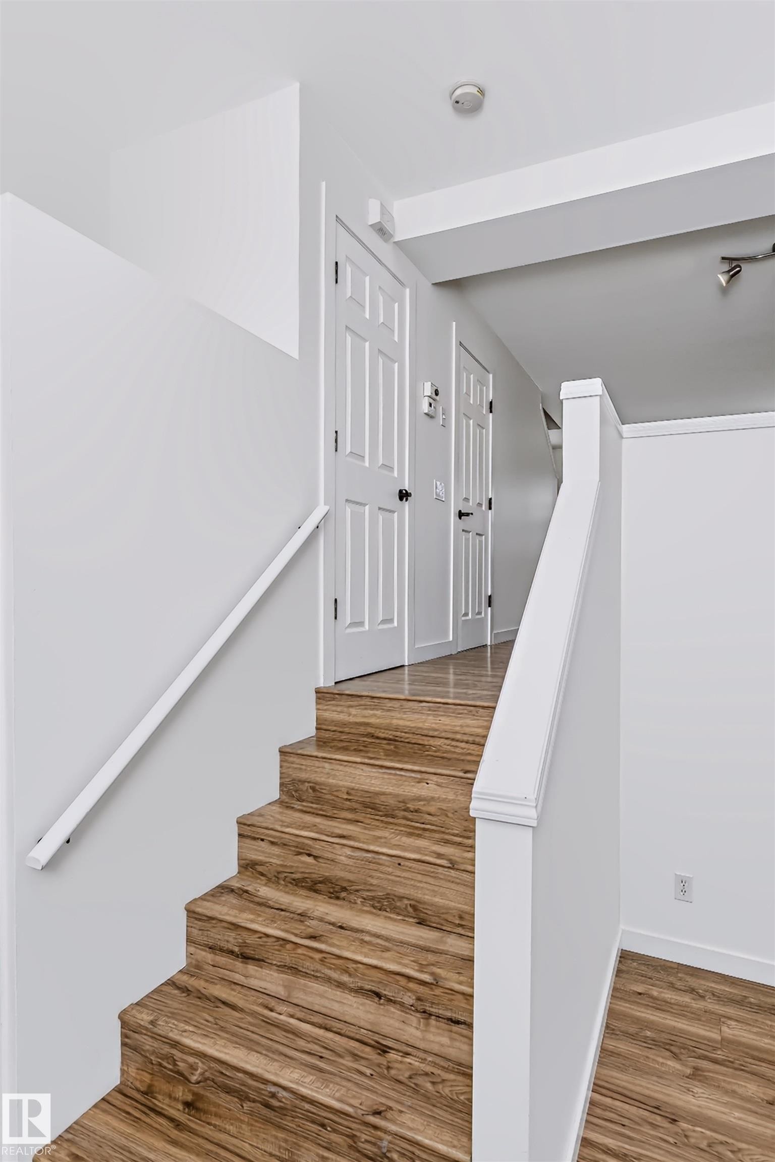 Staircase featuring wood-finish flooring, white risers, and a white handrail - #66 8304 11 Av Sw, Edmonton, AB - Indoor Photo Showing Other Room