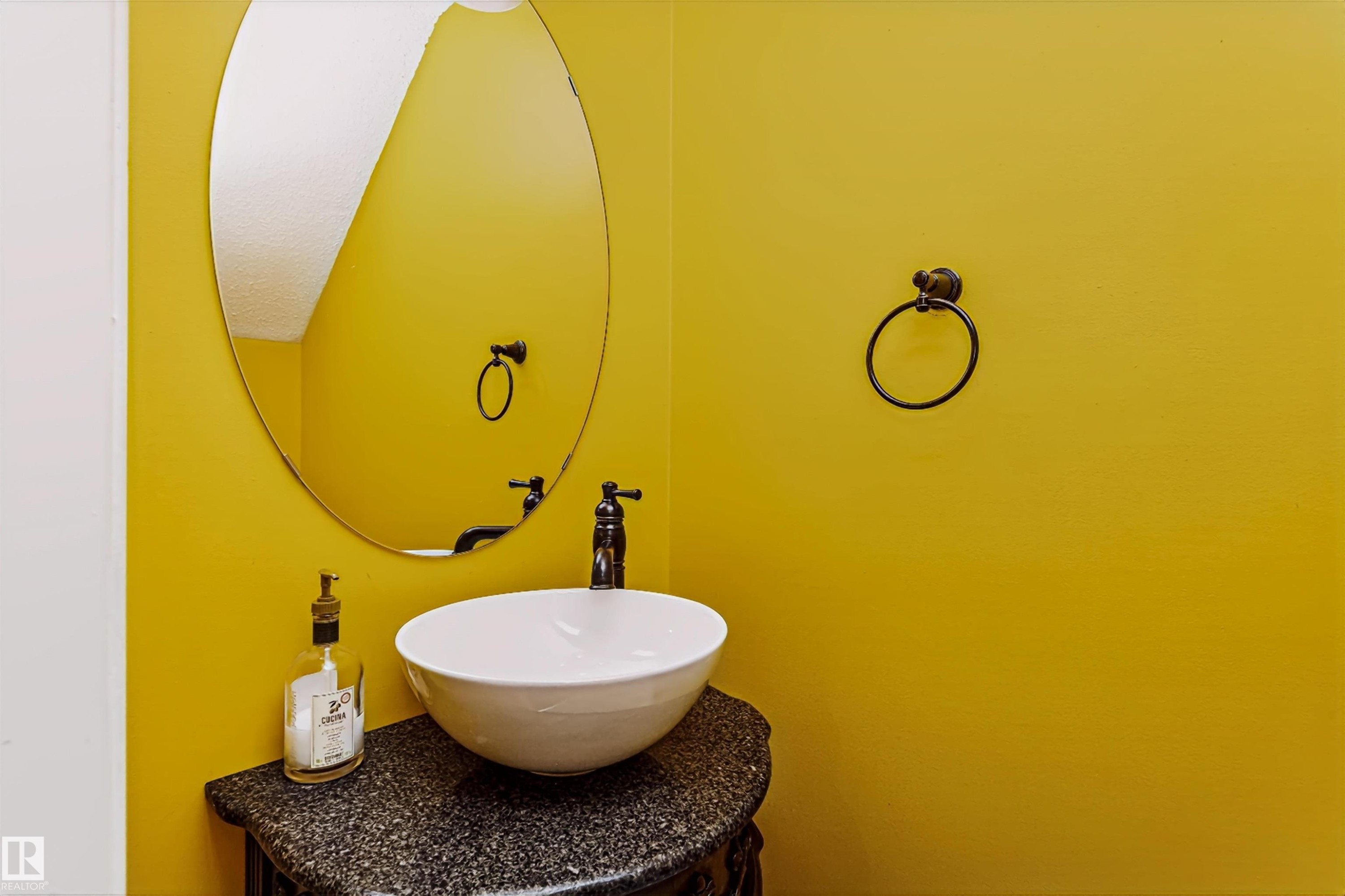 Powder room featuring a vessel sink, dark stone countertop, and an oval wall-mounted mirror - #66 8304 11 Av Sw, Edmonton, AB - Indoor Photo Showing Bathroom