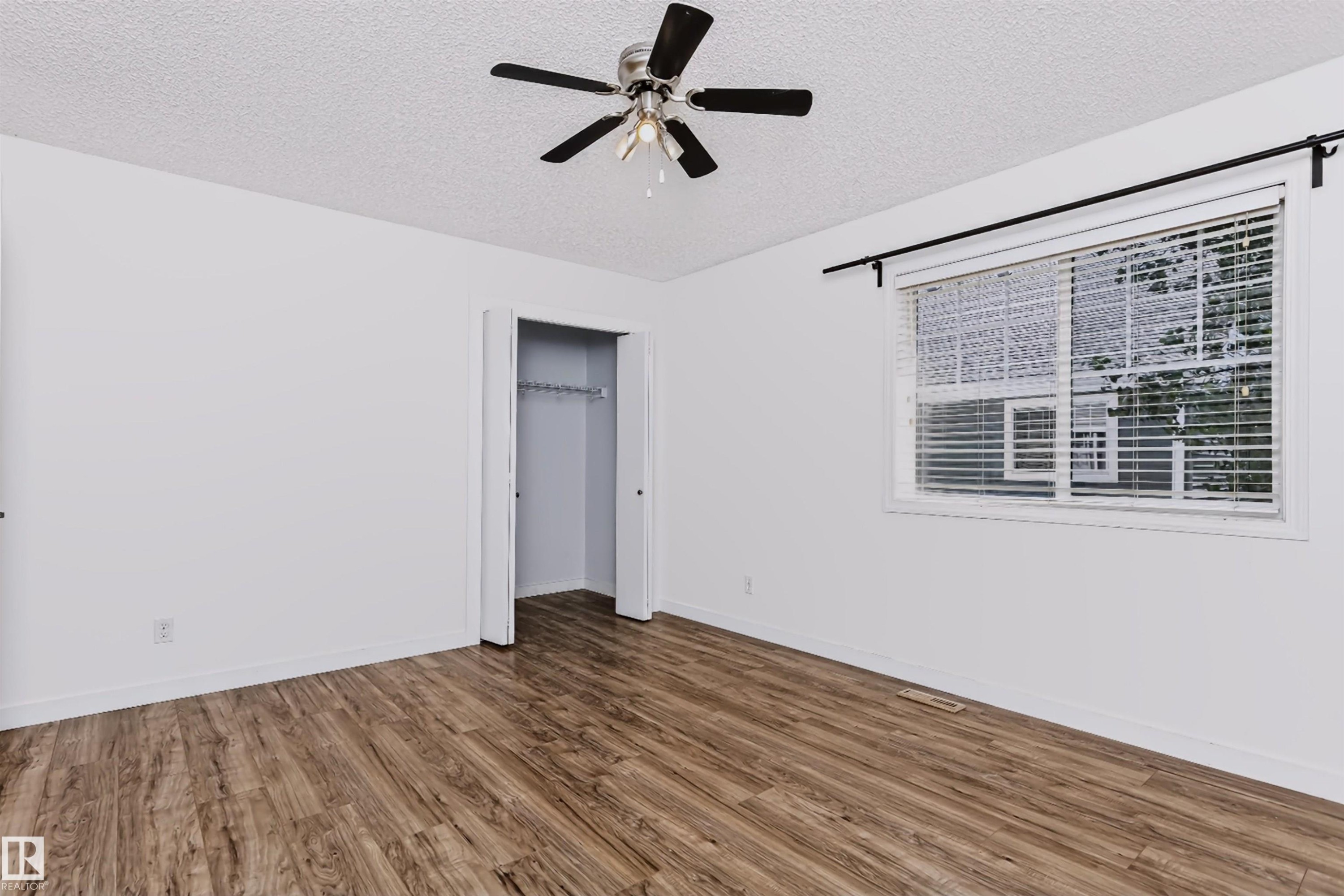 Spacious room featuring wood-finish flooring, a ceiling fan with light fixture, and a large window with blinds - #66 8304 11 Av Sw, Edmonton, AB - Indoor Photo Showing Other Room