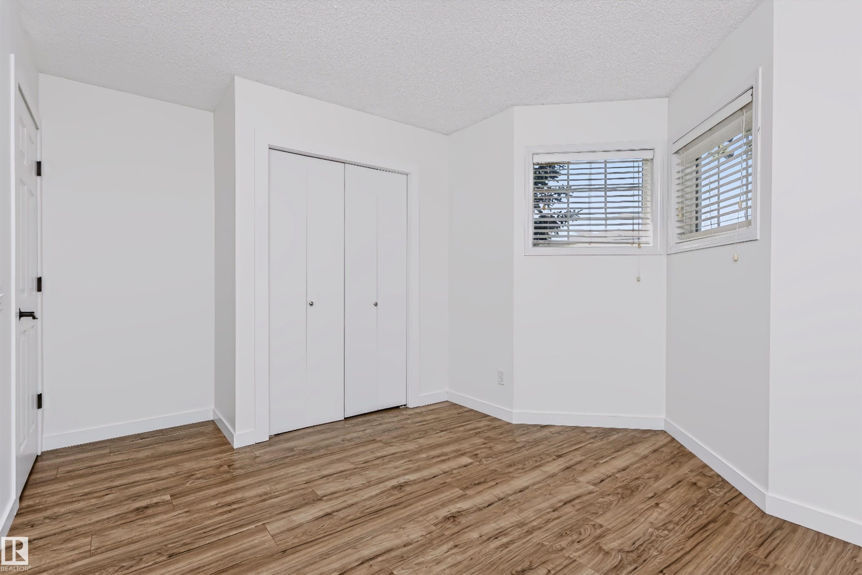 Room with wood-finish flooring, two windows with blinds, and white bi-fold closet doors - #66 8304 11 Av Sw, Edmonton, AB - Indoor Photo Showing Other Room