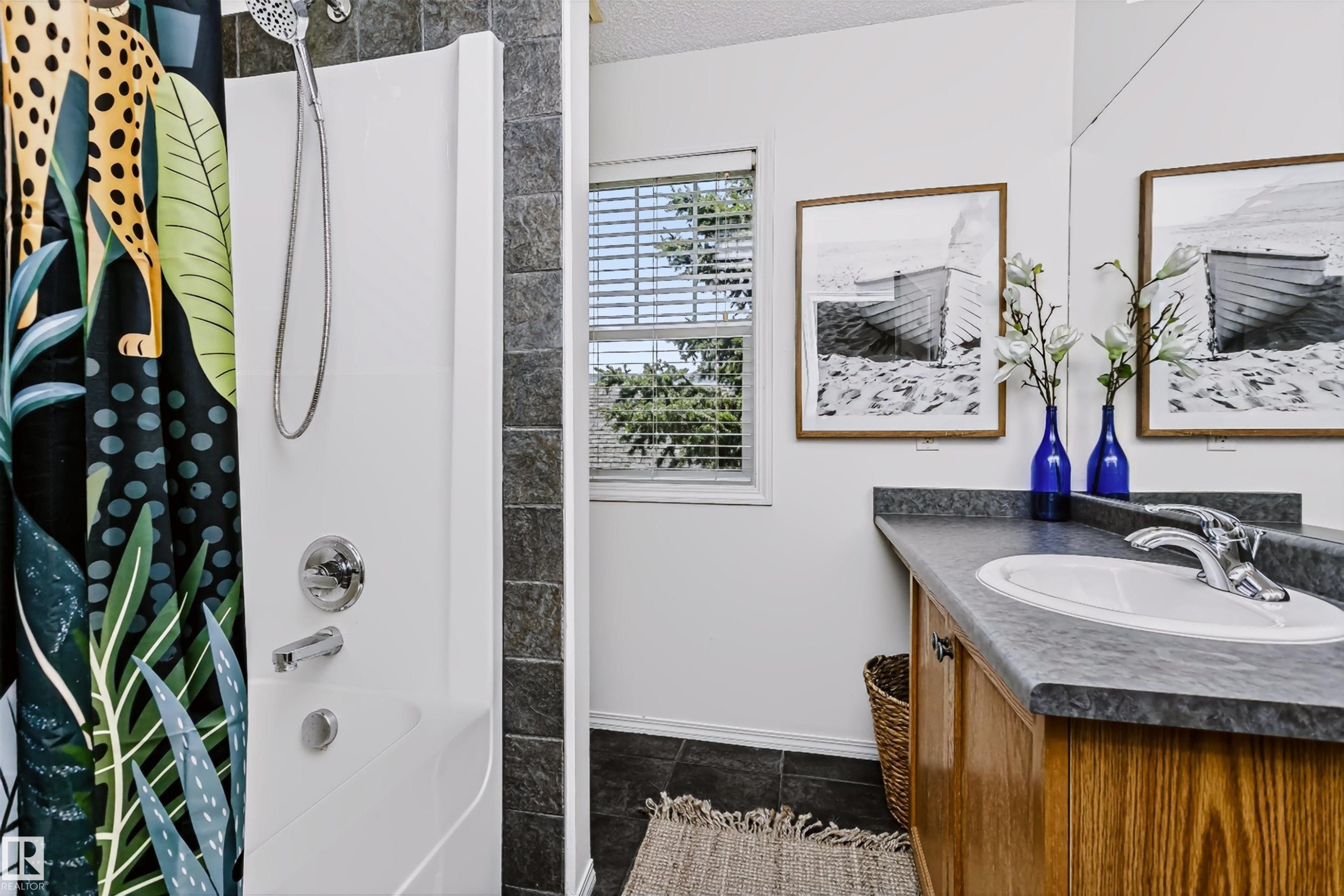 Bathroom with a white shower enclosure, chrome fixtures, and dark tiled walls - #66 8304 11 Av Sw, Edmonton, AB - Indoor Photo Showing Bathroom