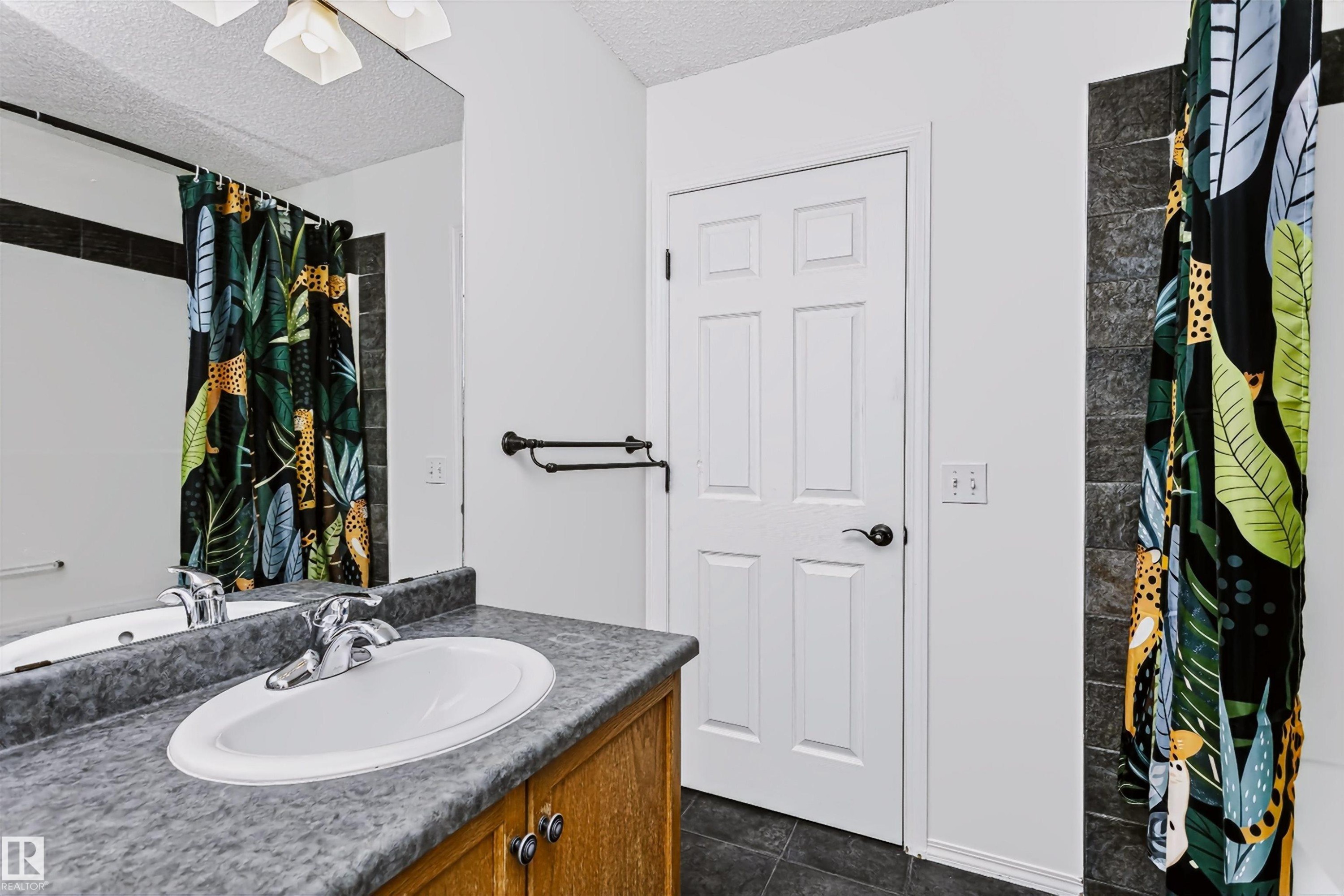 Bathroom featuring a wood-finish vanity with a single basin sink, laminate countertop, and chrome faucet - #66 8304 11 Av Sw, Edmonton, AB - Indoor Photo Showing Bathroom