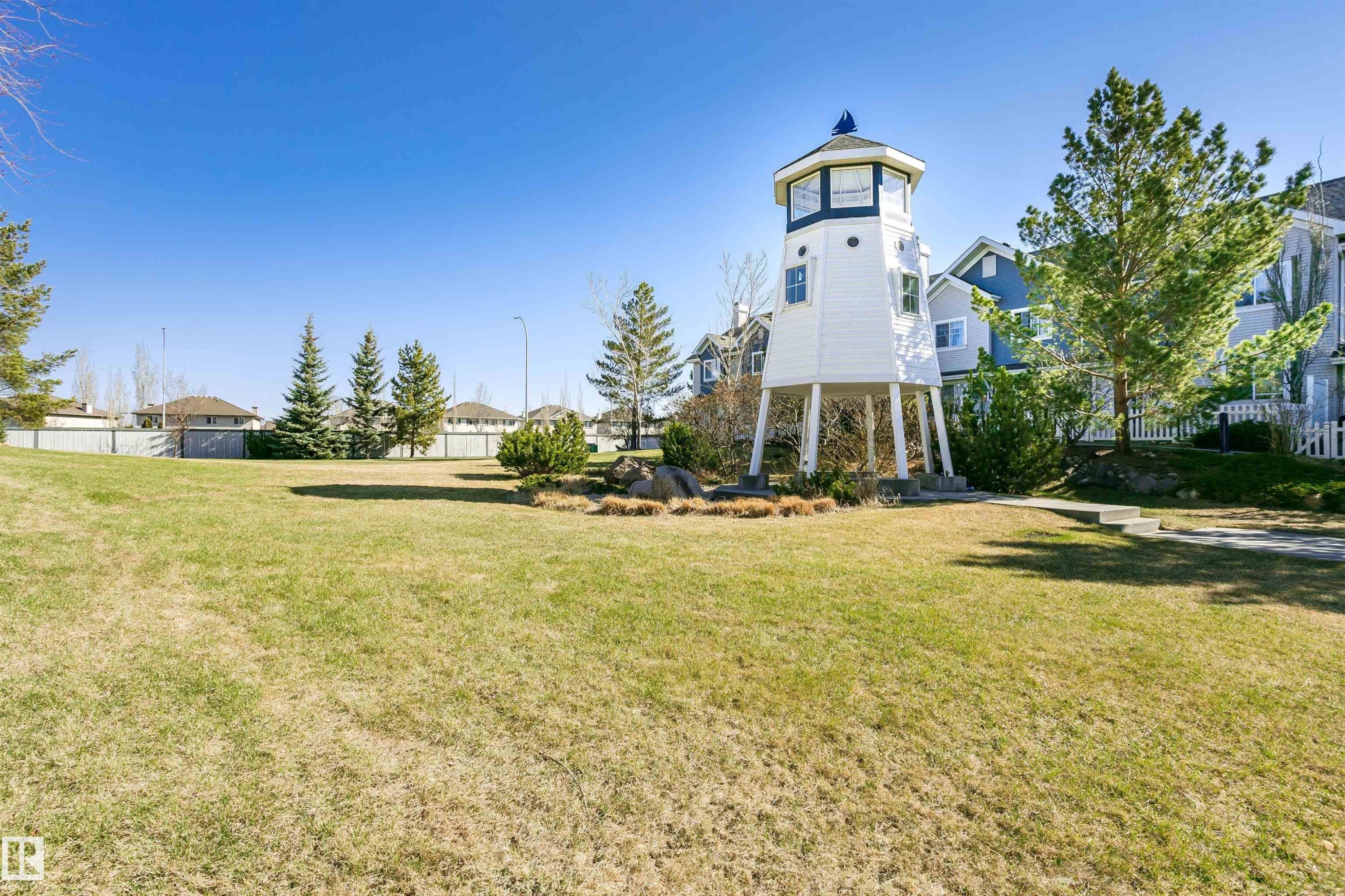 Expansive green space featuring a distinctive lighthouse-inspired structure with white siding and a blue roof accent - #66 8304 11 Av Sw, Edmonton, AB - Outdoor