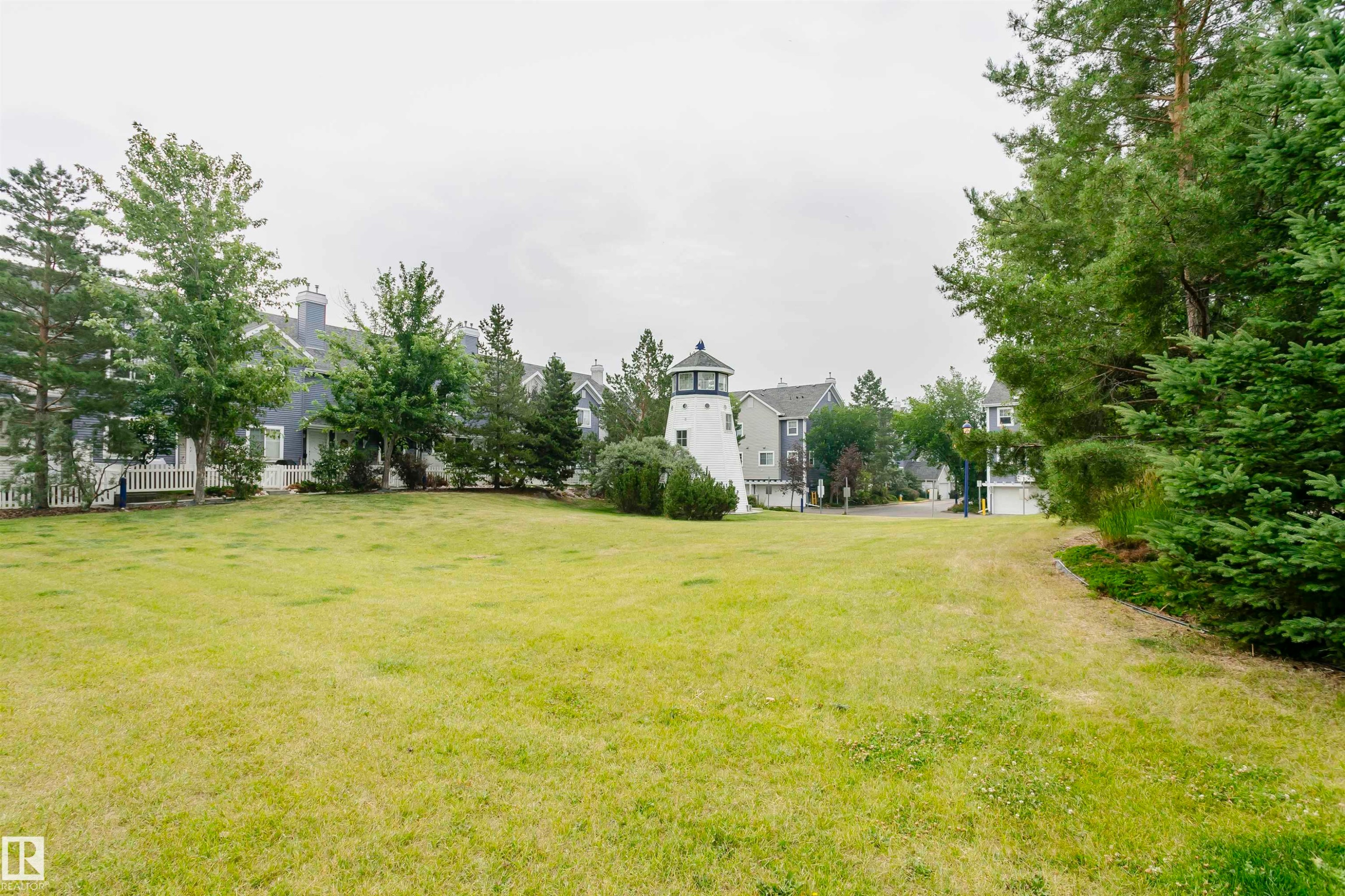 Expansive green space featuring a prominent decorative lighthouse structure, surrounded by established trees and residential buildings - #66 8304 11 Av Sw, Edmonton, AB - Outdoor